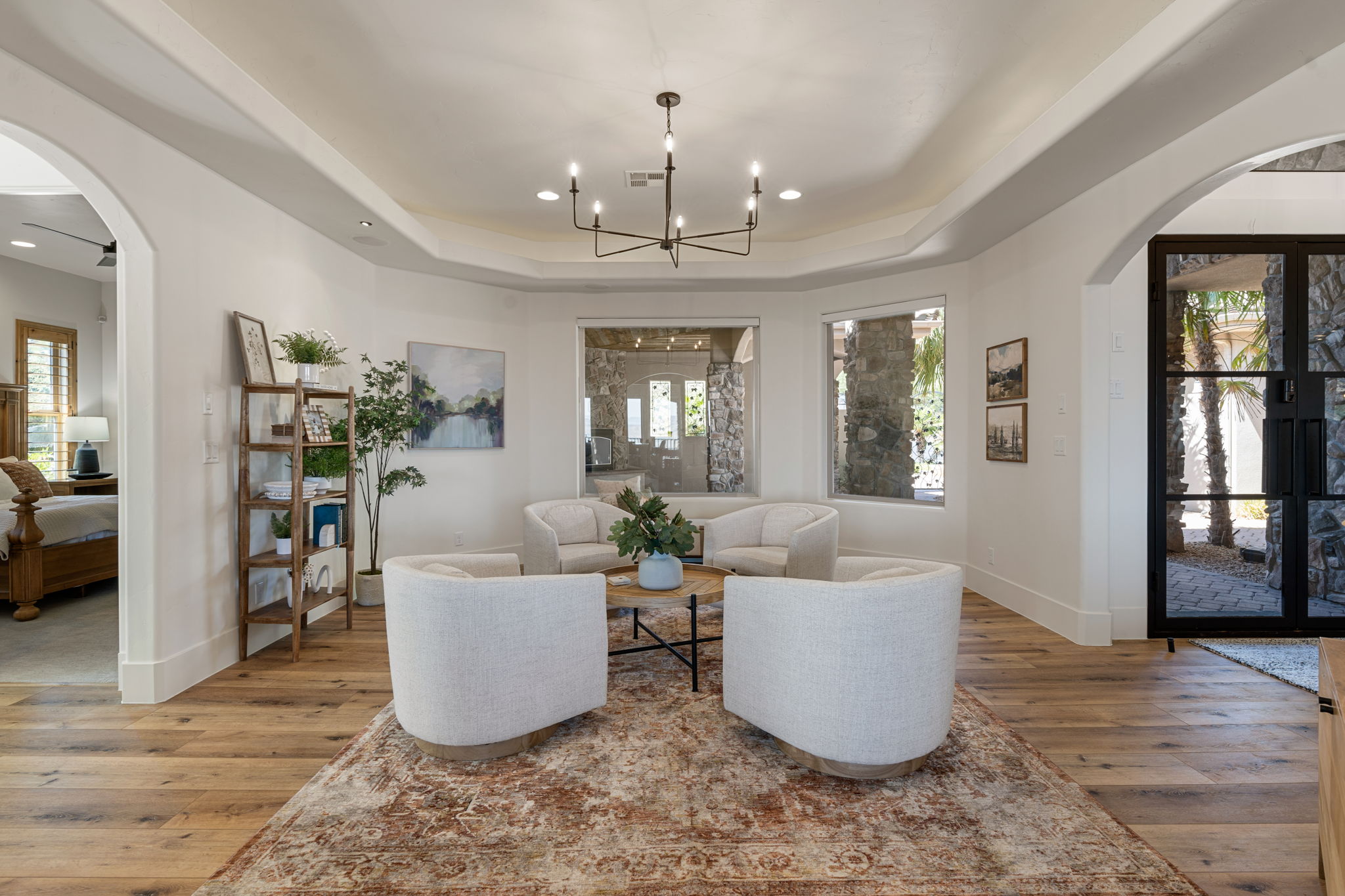 Spacious living area featuring wood-finish flooring, a tray ceiling with a contemporary chandelier, and large windows