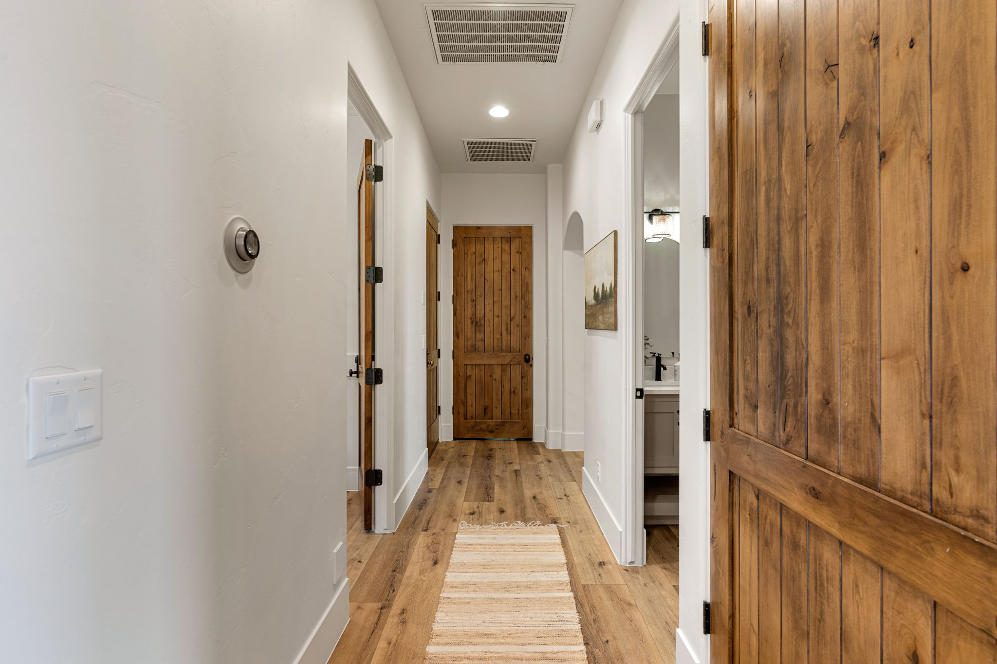 Hallway featuring wood-finish flooring, white walls, recessed lighting, and solid wood doors with dark hardware