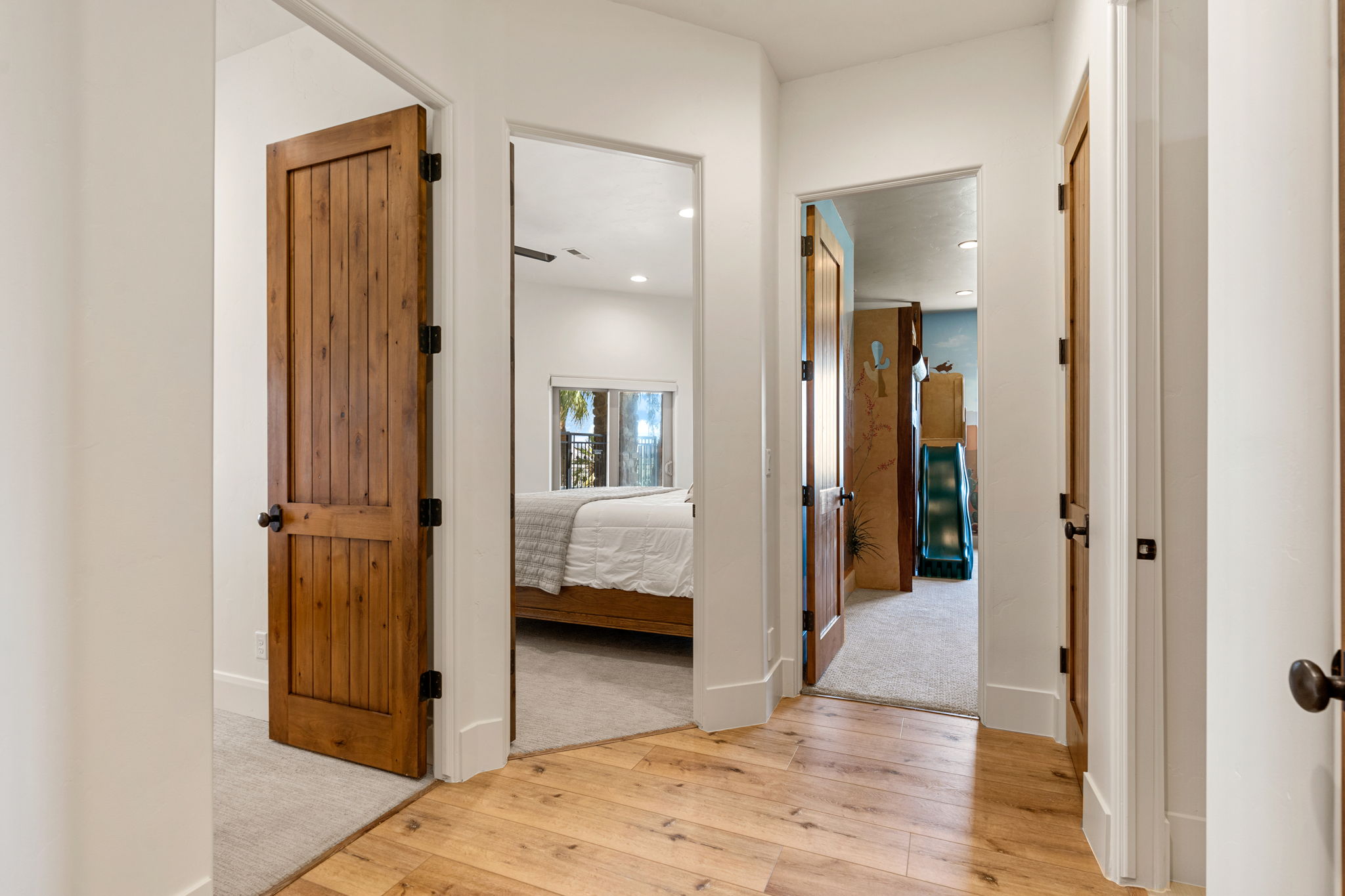 Hallway featuring wood-finish flooring, white walls, and multiple solid wood paneled doors with dark hardware