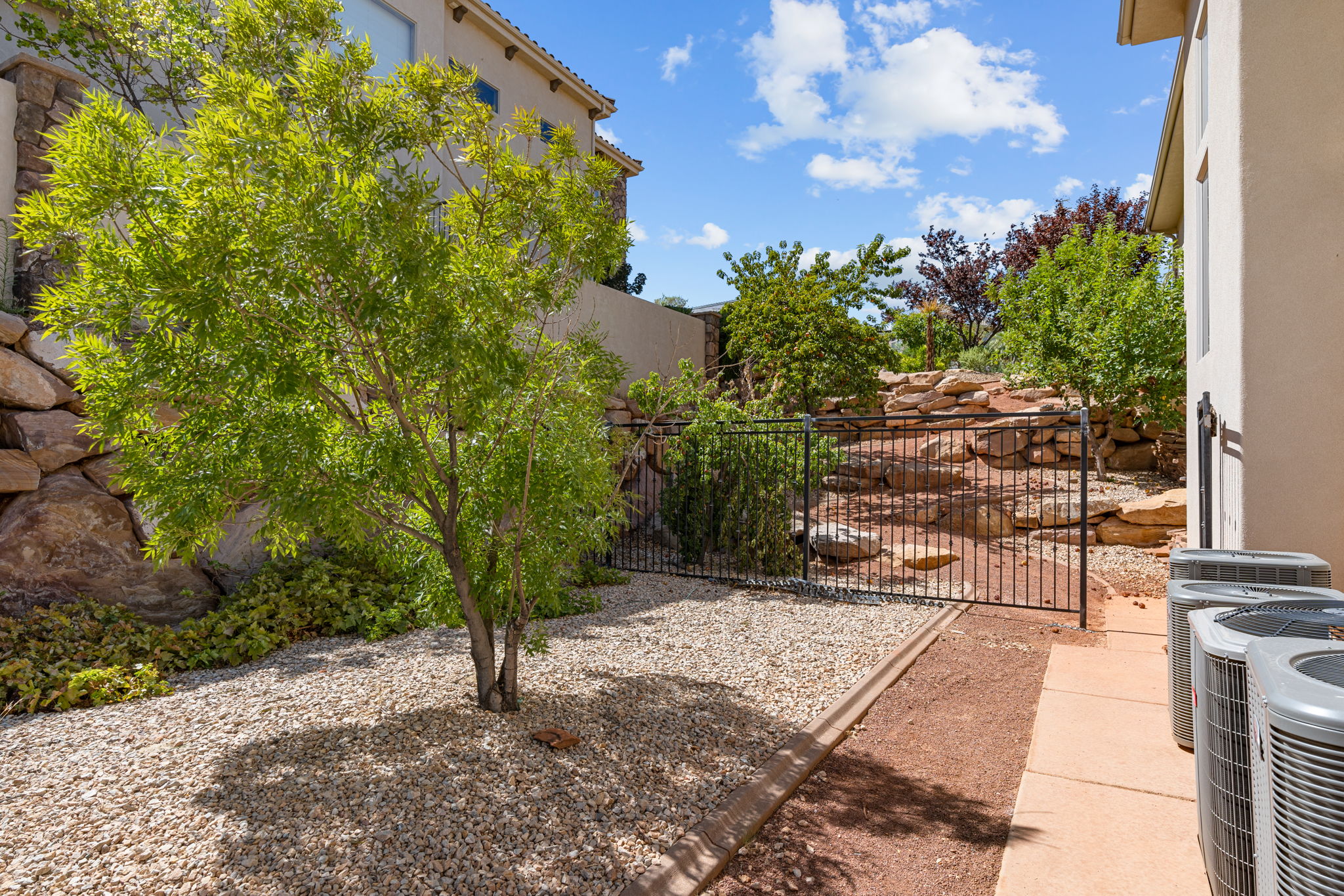 Exterior landscaping featuring decorative gravel, a mature tree, and a black wrought iron fence