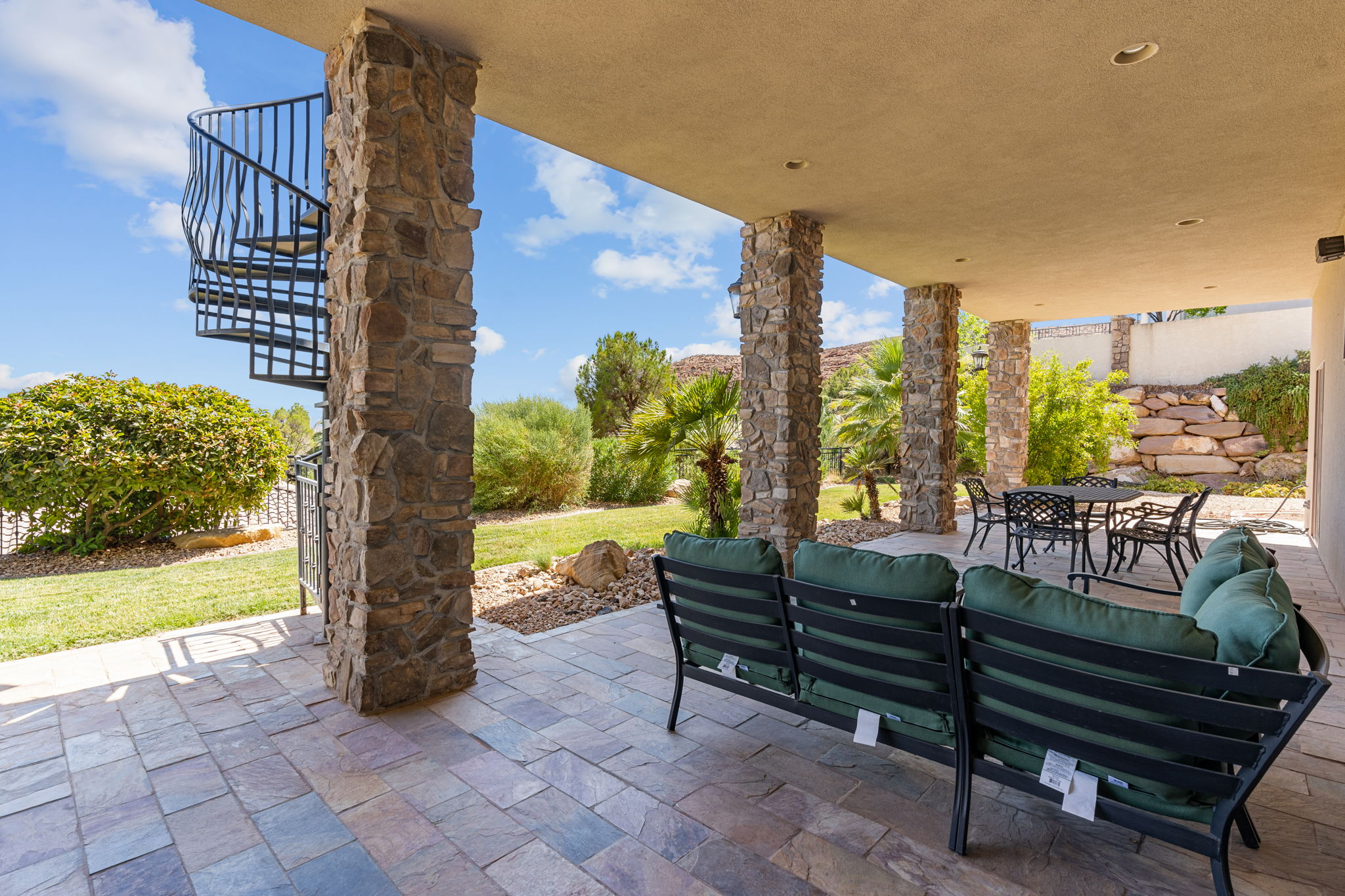 Expansive covered patio featuring stone-clad columns, a spiral staircase, and stone paver flooring