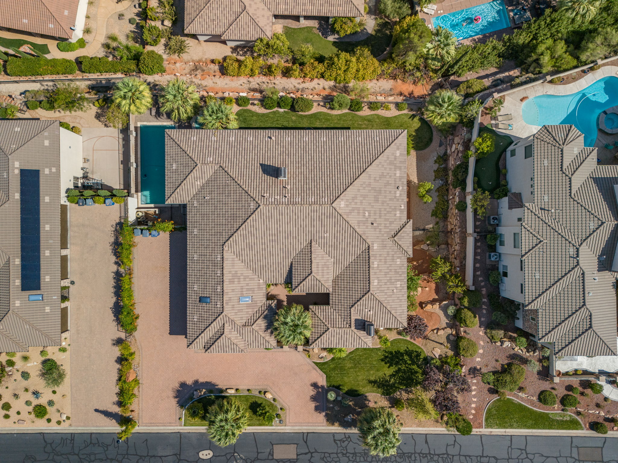 Expansive property featuring a tiled roof, a large swimming pool, mature palm trees, a brick paver driveway, and varied landscaping
