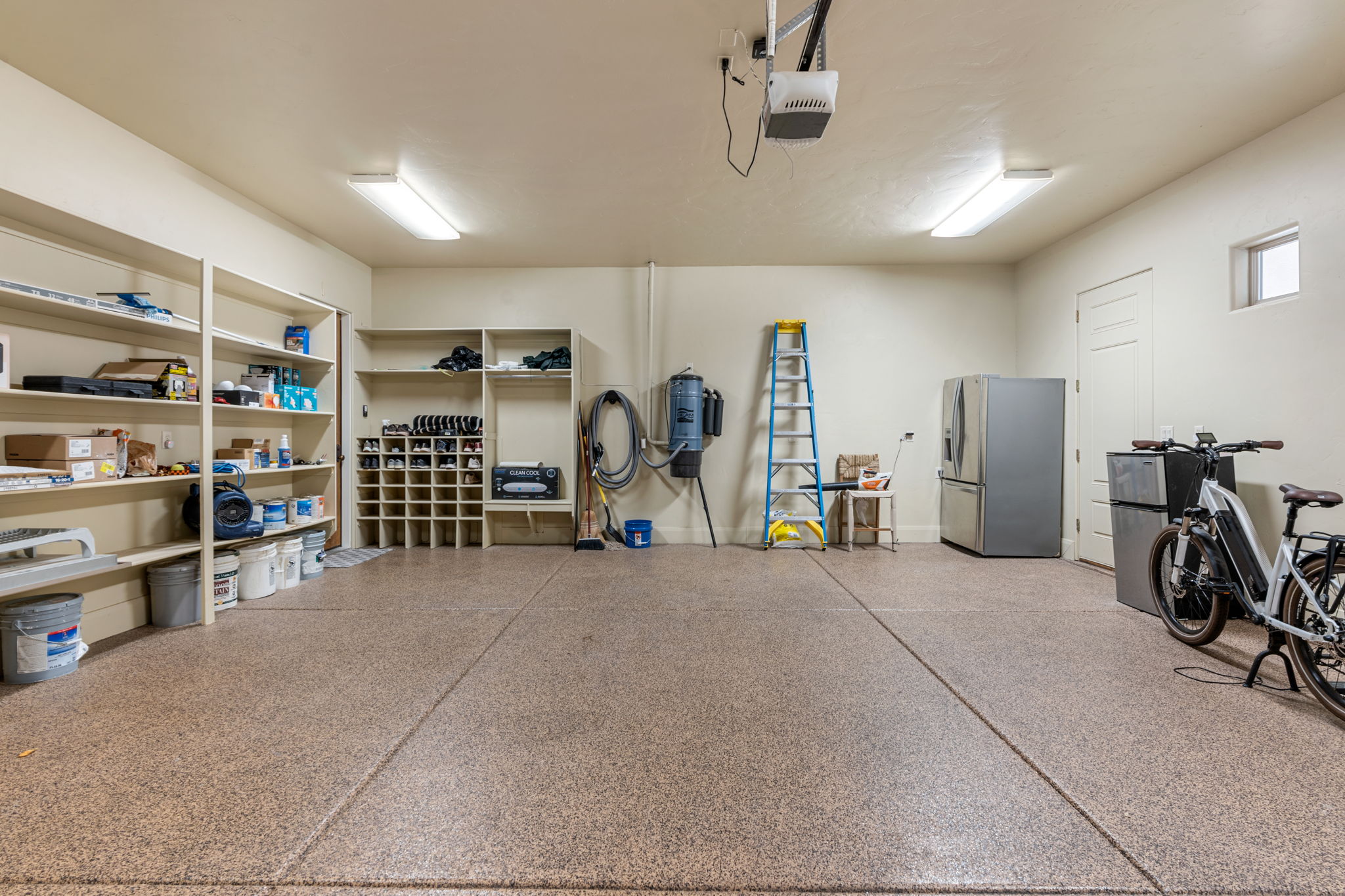 Epoxy-coated garage flooring featuring fluorescent lighting, built-in shelving, and a side-access door