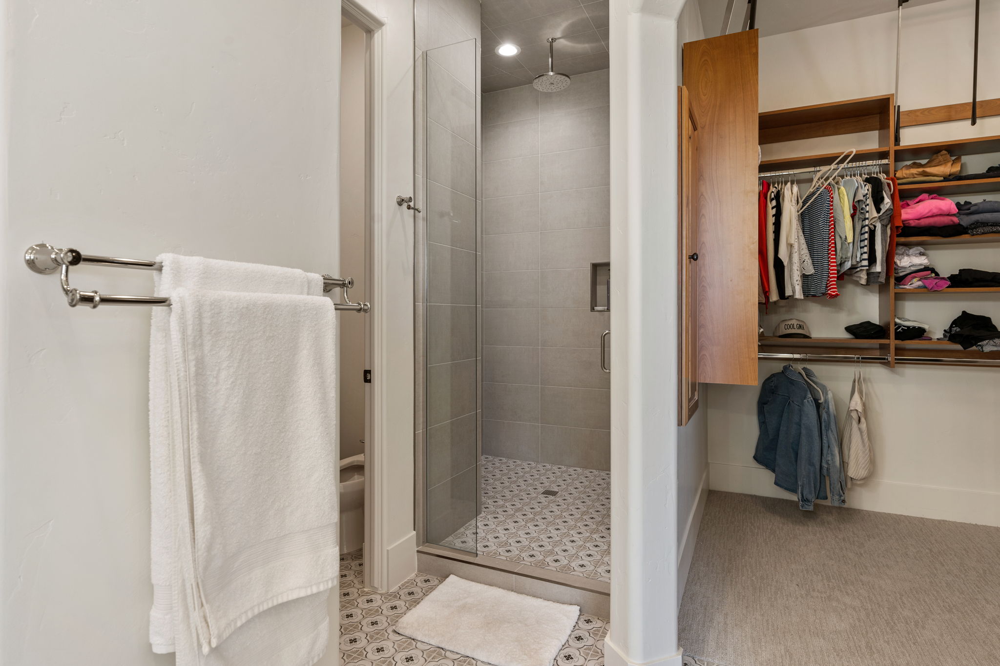 Walk-in shower with glass enclosure, rain showerhead, recessed shelf, and patterned floor tile