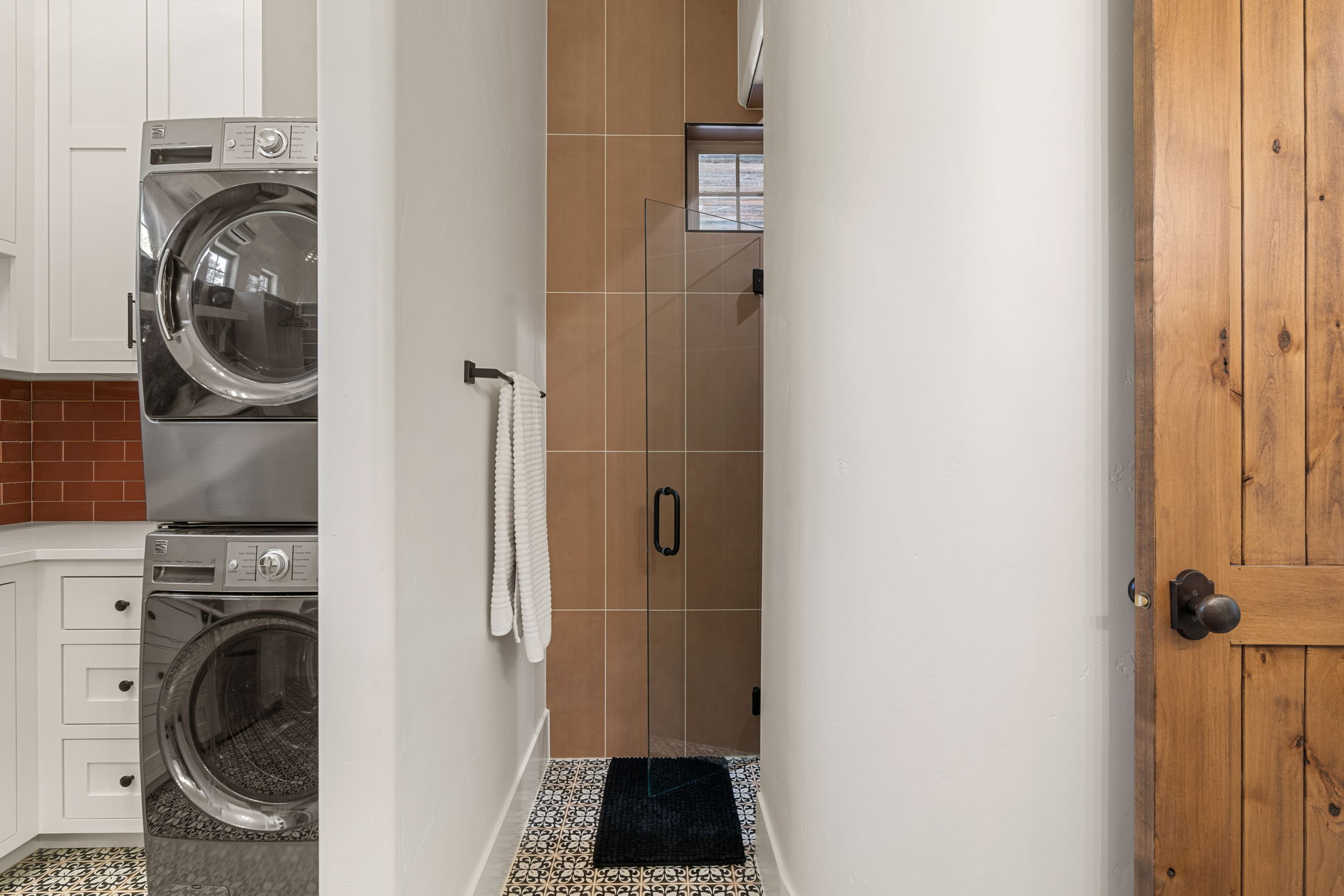 Laundry area featuring stacked stainless-steel appliances, white cabinetry, and a red subway tile backsplash