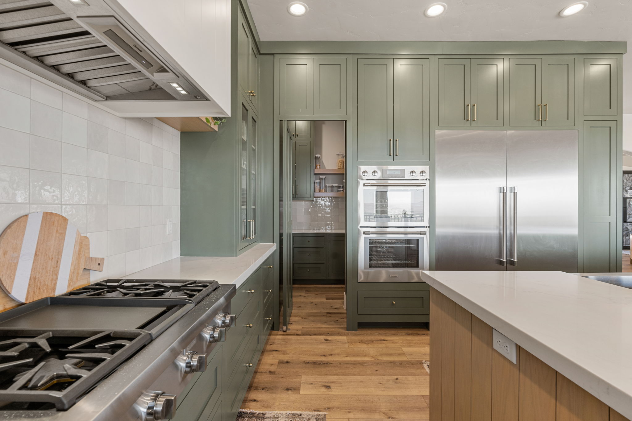 Kitchen featuring sage green cabinetry, stainless steel appliances, light wood-finish flooring, white subway tile backsplash, and light-toned countertops