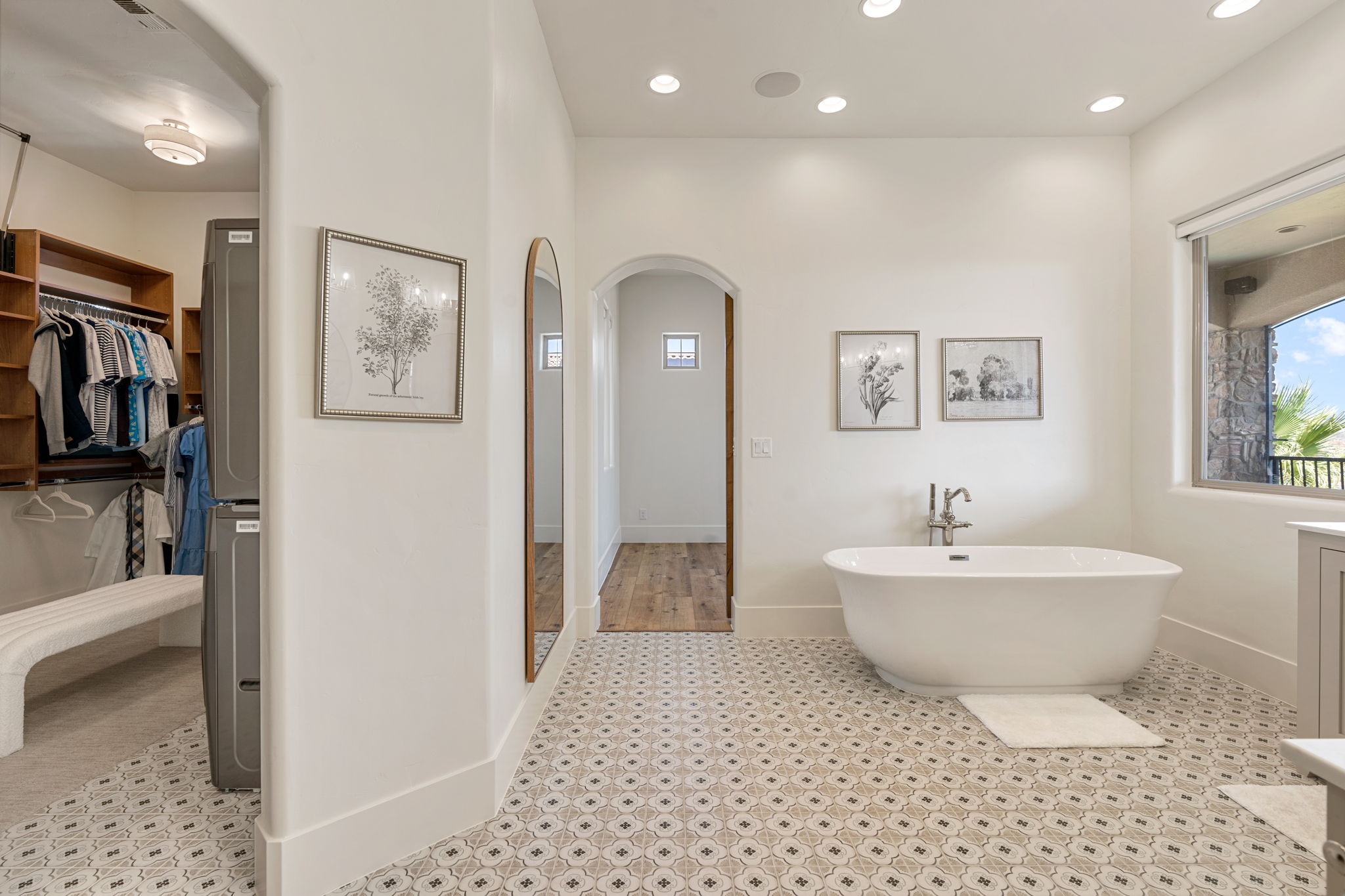 Spacious bathroom featuring patterned floor tiling, a freestanding soaking tub with a floor-mounted faucet, and a large window