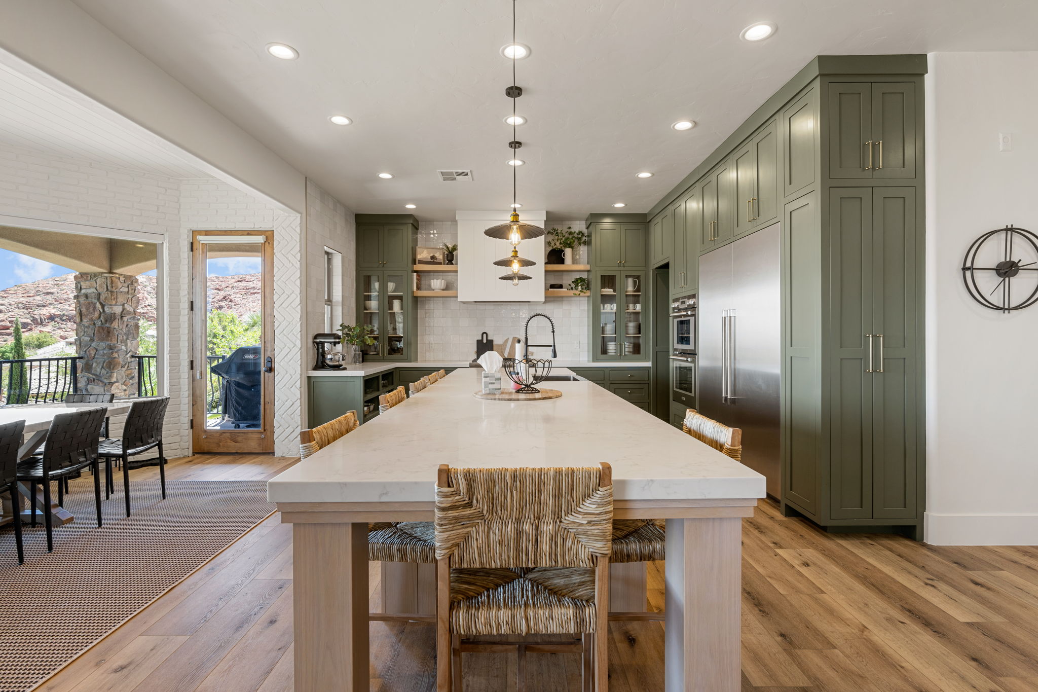 Spacious kitchen featuring a long central island with seating, extensive green cabinetry, wood-finish flooring, recessed lighting, and stainless steel appliances