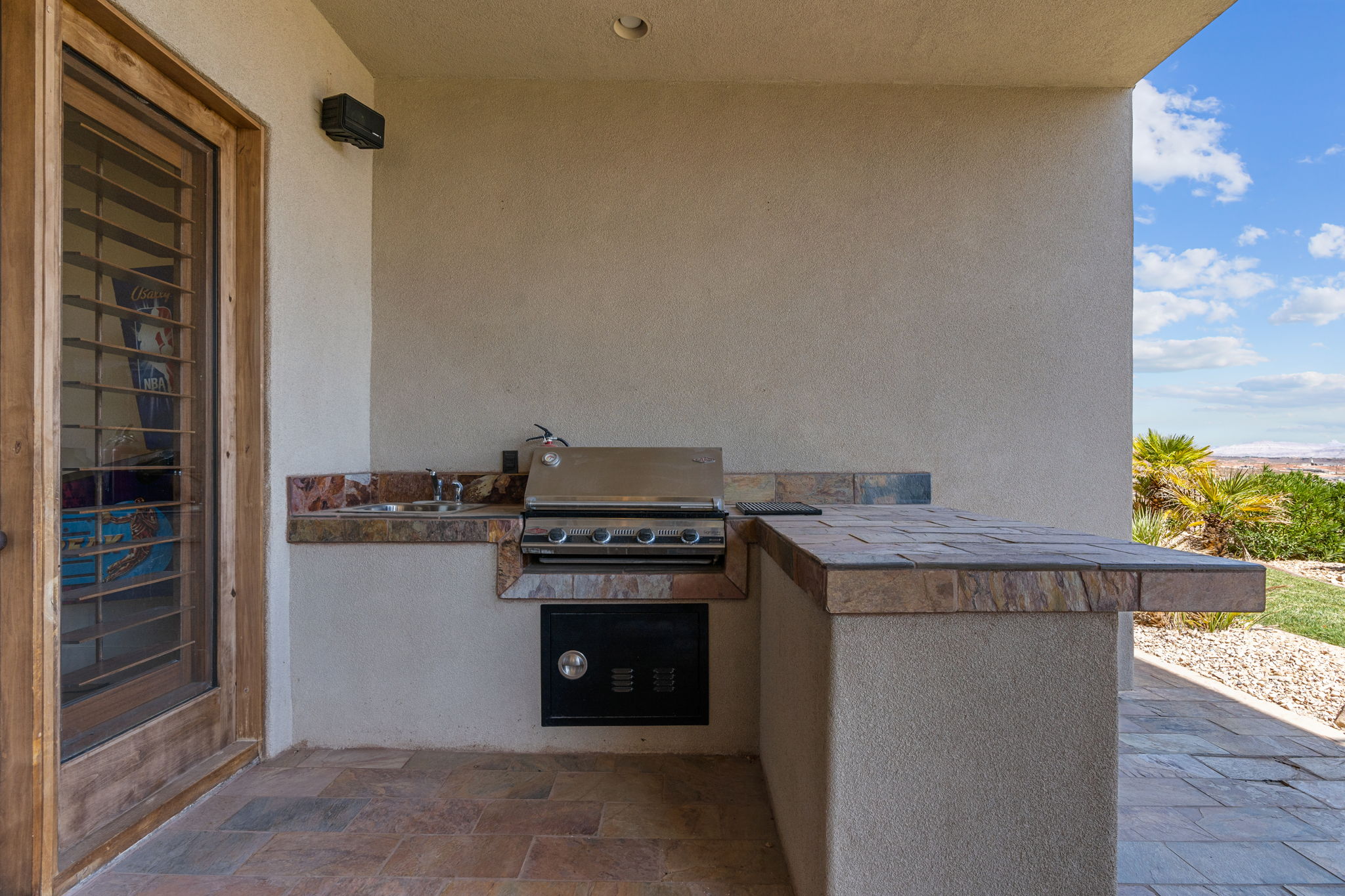 Outdoor kitchen featuring a built-in stainless steel grill, integrated sink, stone-finish countertops, and matching tile flooring