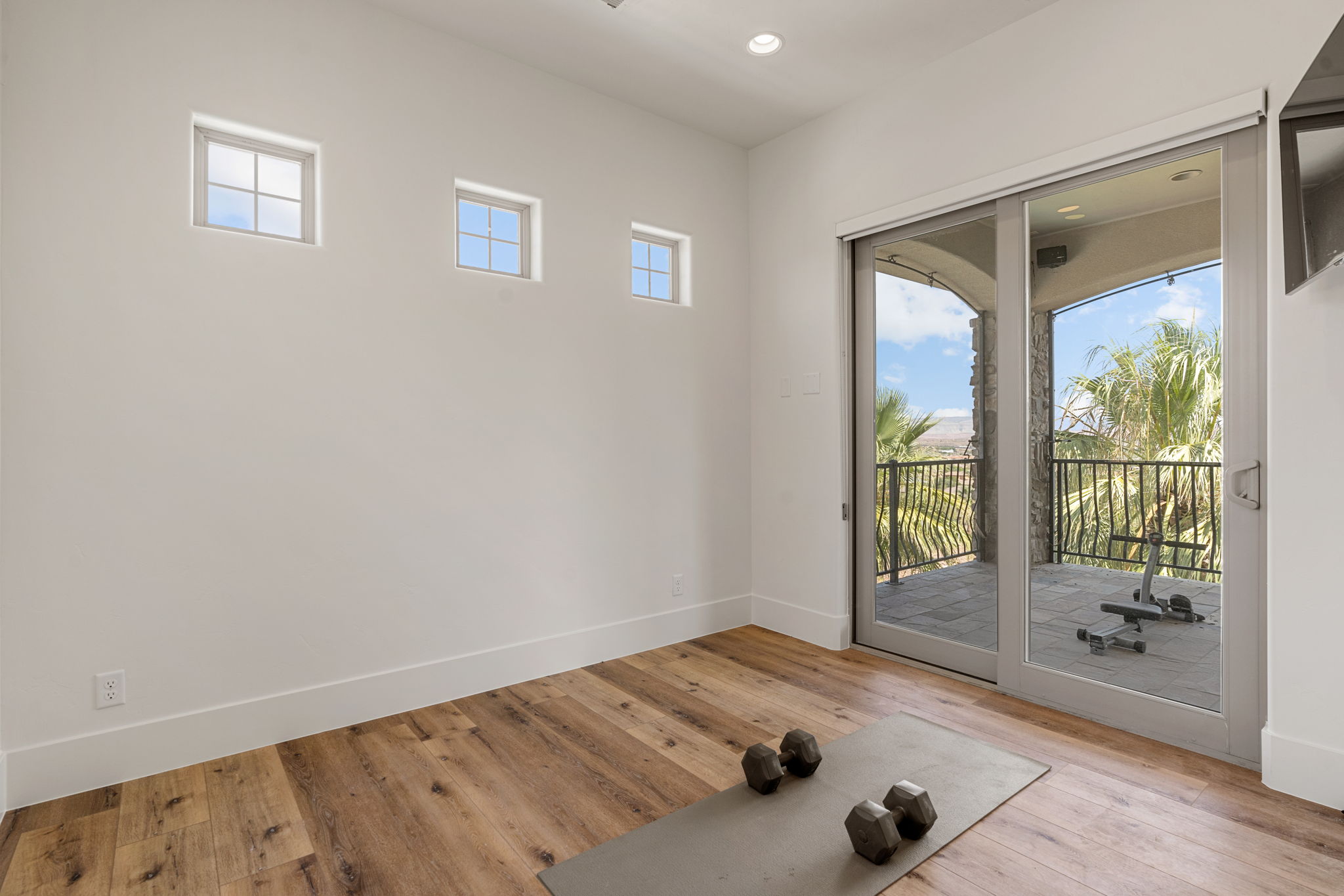 Spacious interior room featuring wood-finish flooring, high ceilings with recessed lighting, and a sliding glass door opening to a private balcony