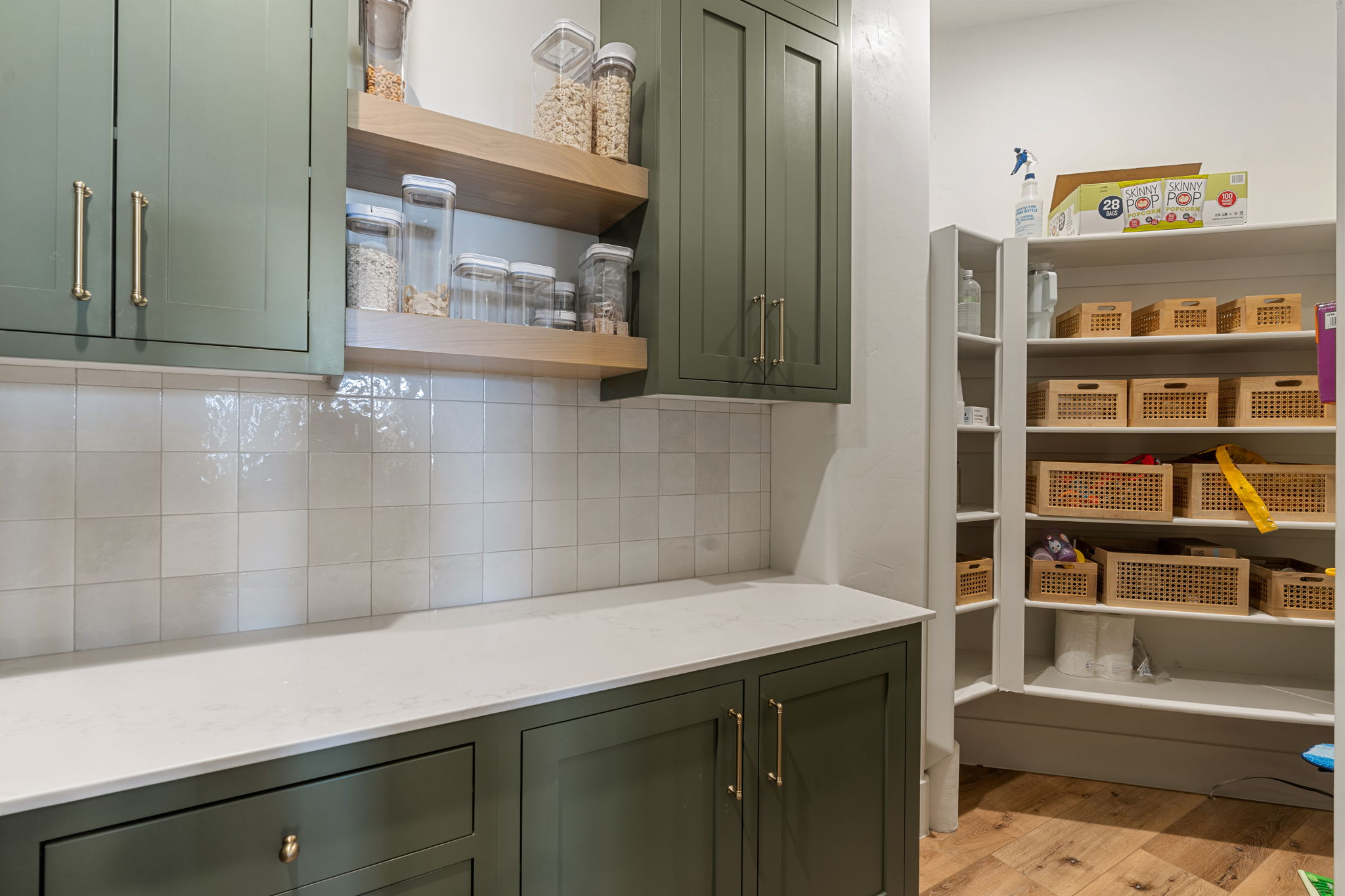 Kitchen pantry featuring olive green cabinetry, light stone countertops, white square tile backsplash, and open wood shelving