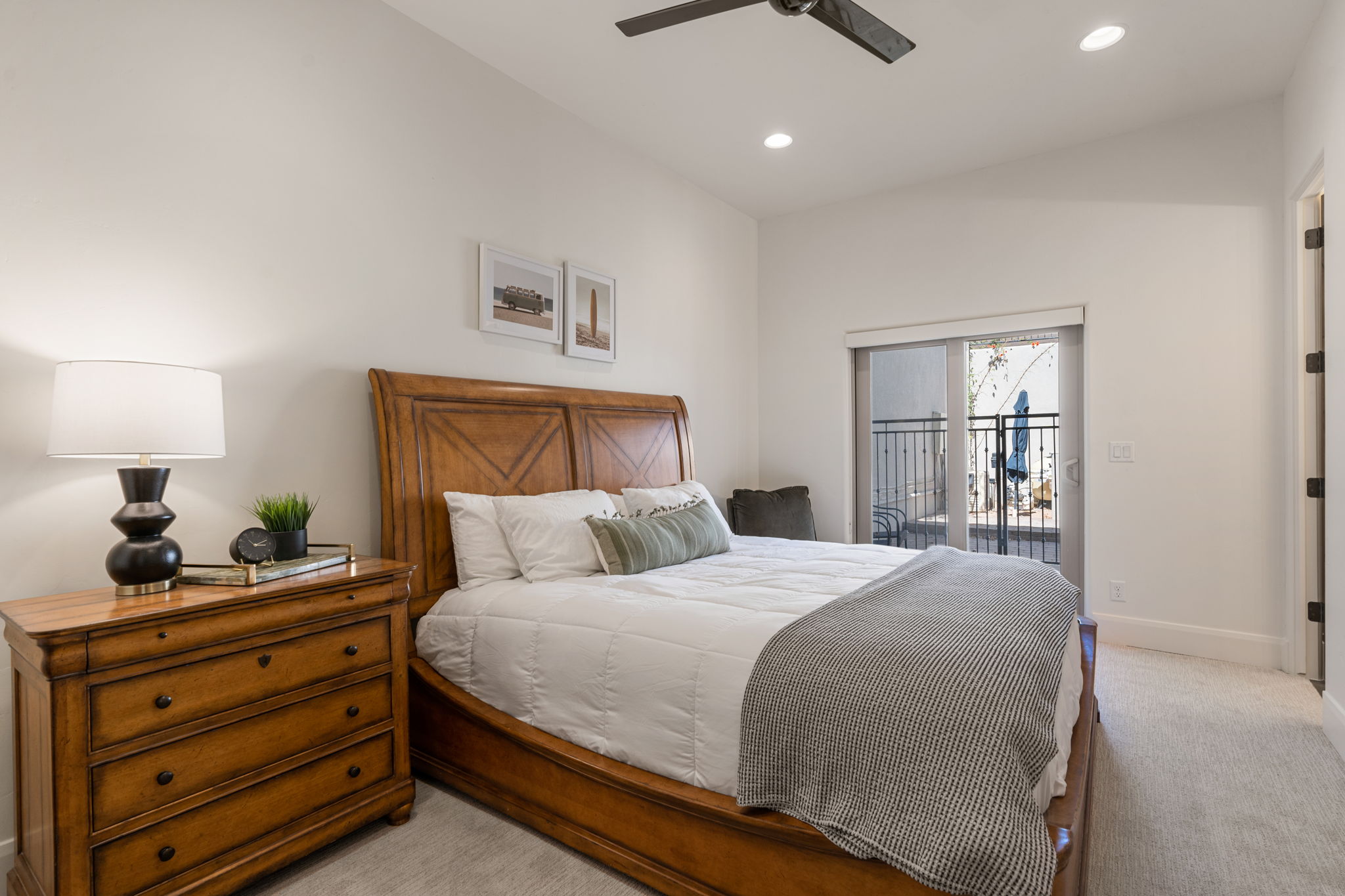Vaulted ceiling with recessed lighting and a ceiling fan, plush carpet flooring, and a sliding glass door leading to an exterior balcony with wrought iron railing