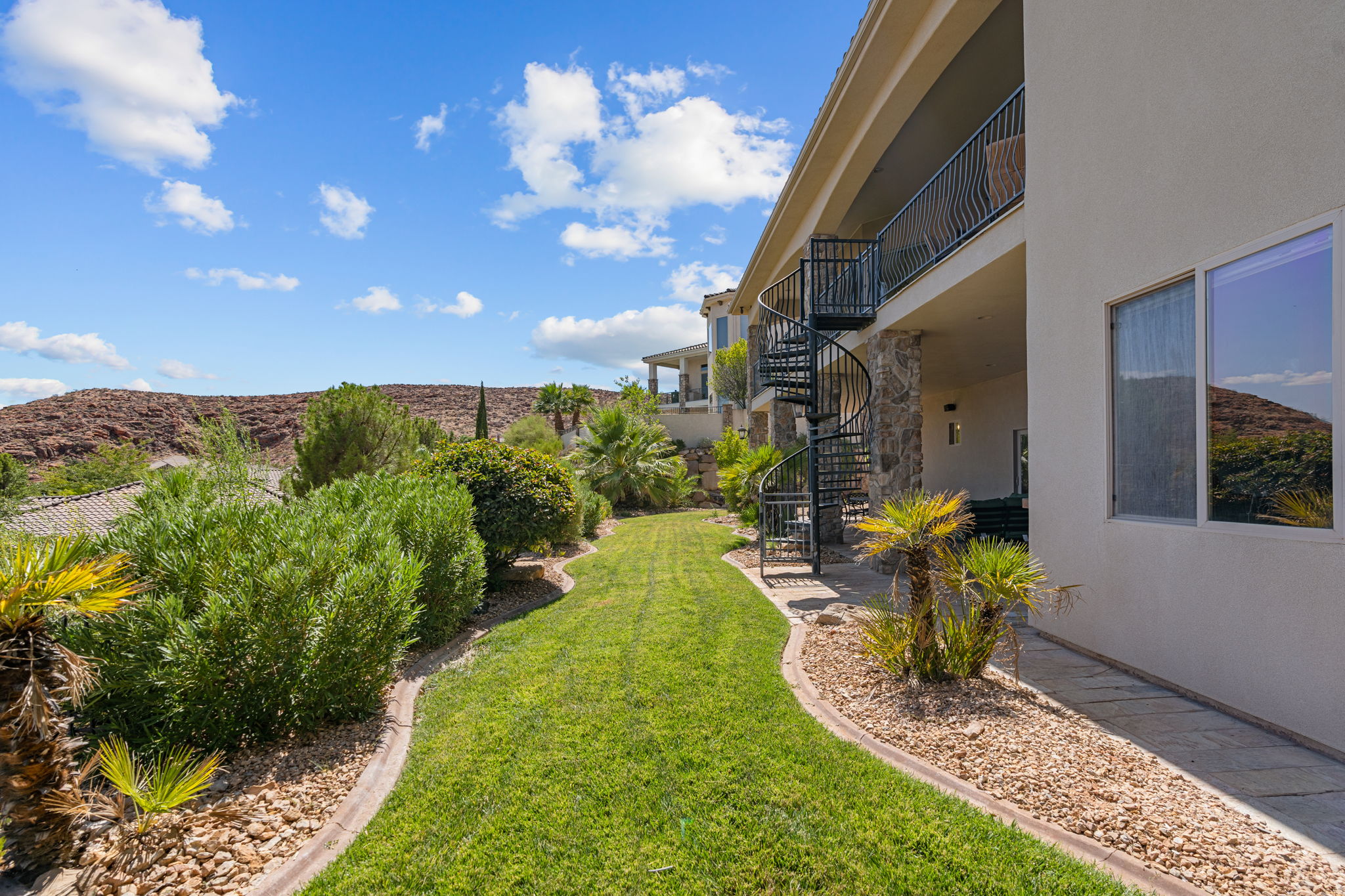 Landscaped backyard featuring a winding lawn, mature desert plantings, and a spiral staircase providing access to an upper-level balcony