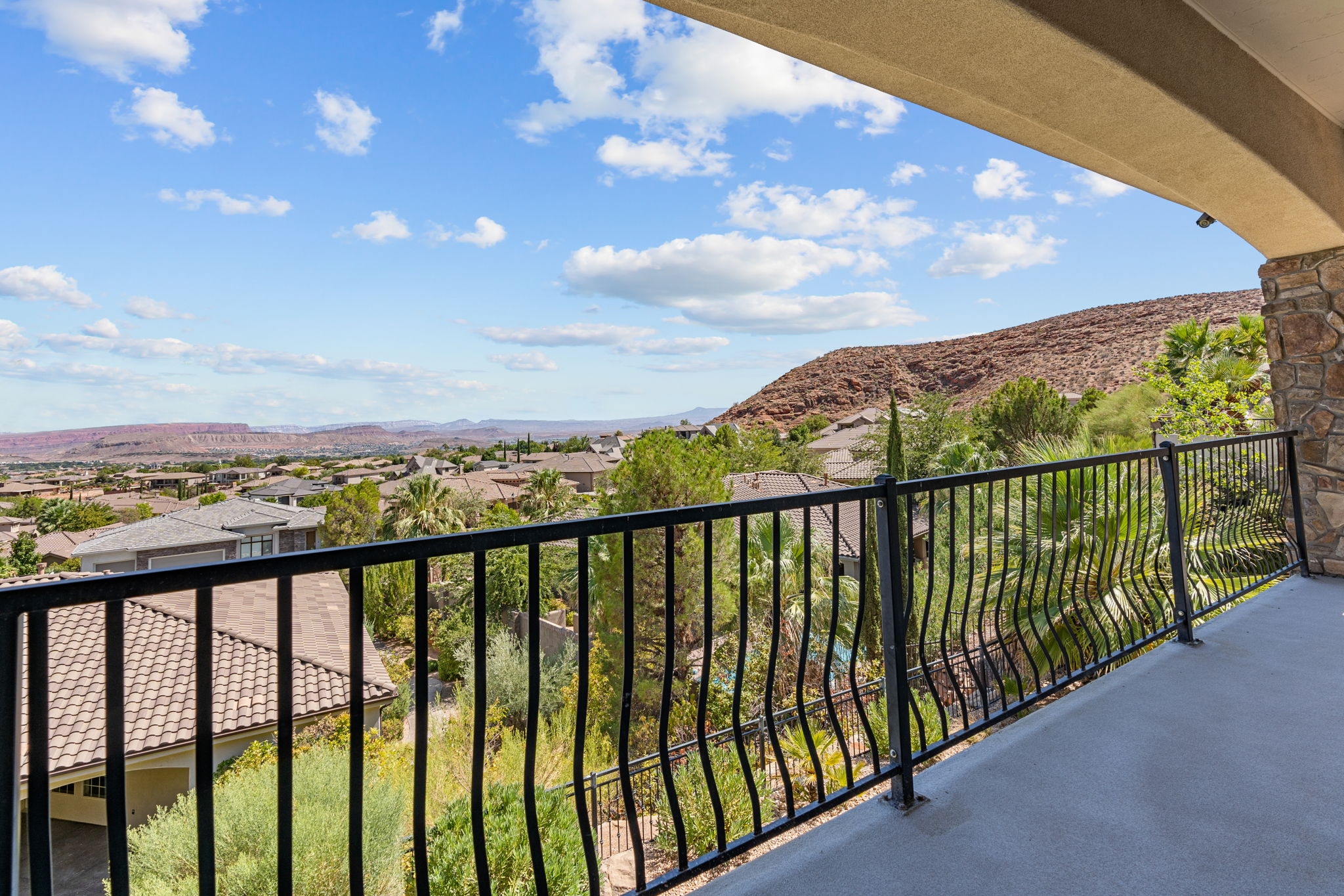 Curved balcony featuring a stone pillar, wrought iron railing, and expansive mountain scenery