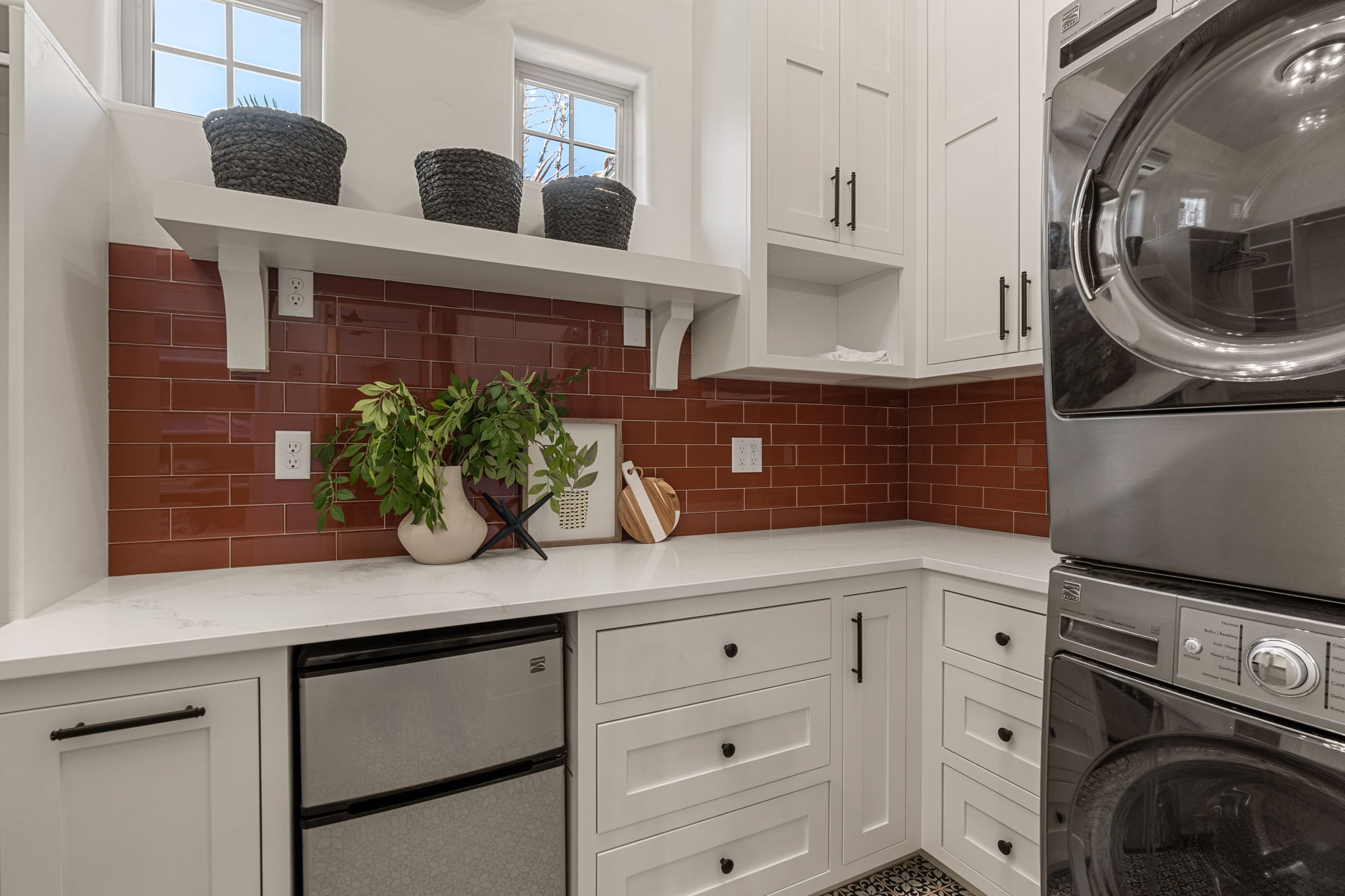 Laundry area featuring white cabinetry, a red subway tile backsplash, white countertops, built-in undercounter refrigeration, and a stackable washer and dryer set
