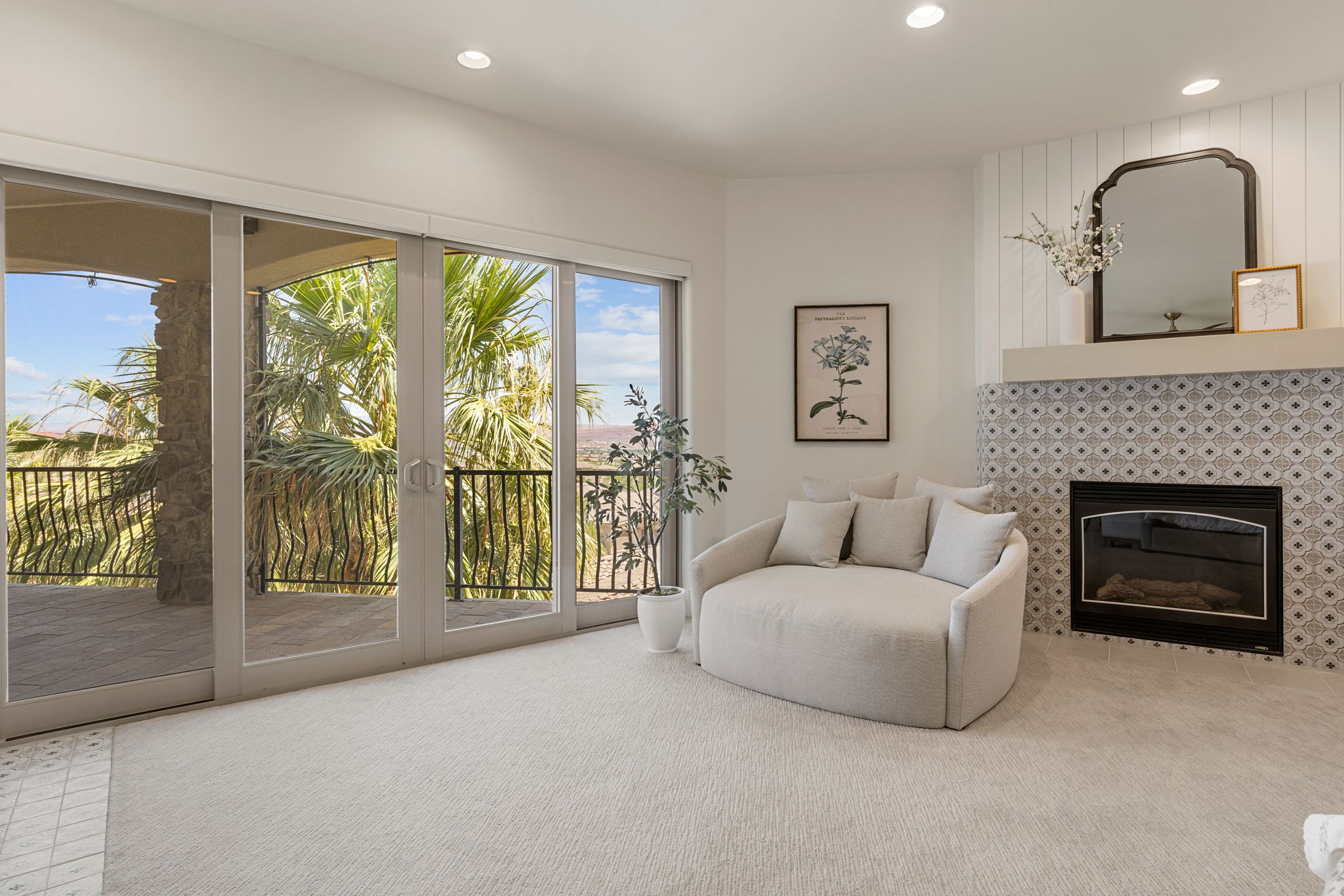 Spacious room featuring multiple sliding glass doors opening to an outdoor balcony with a wrought iron railing, a fireplace with patterned tile surround and white mantel, recessed lighting, and light-colored carpeting