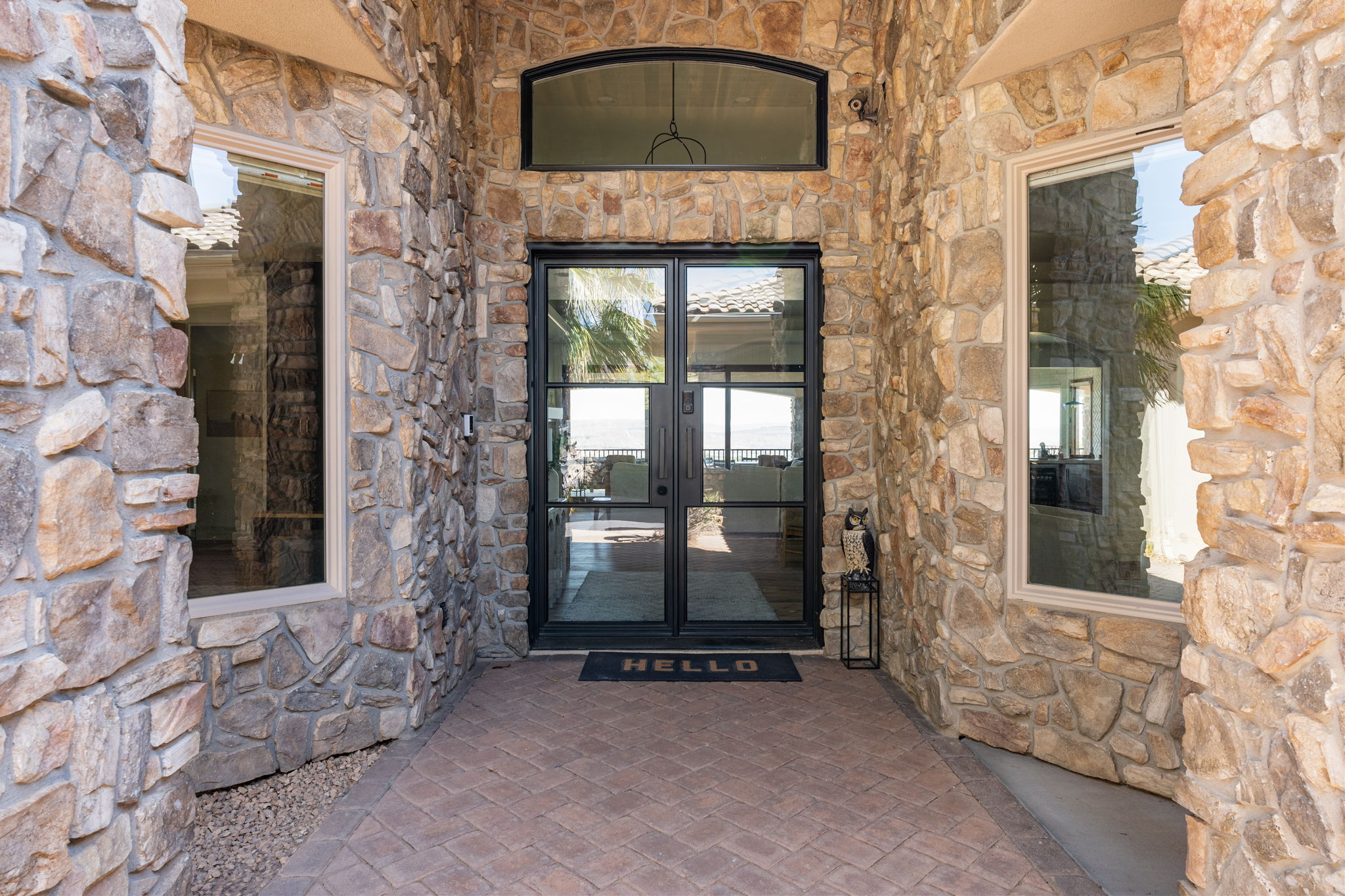 Stone veneer exterior featuring a black-framed glass double entry door, two side windows with tan trim, a transom window, and a paver walkway