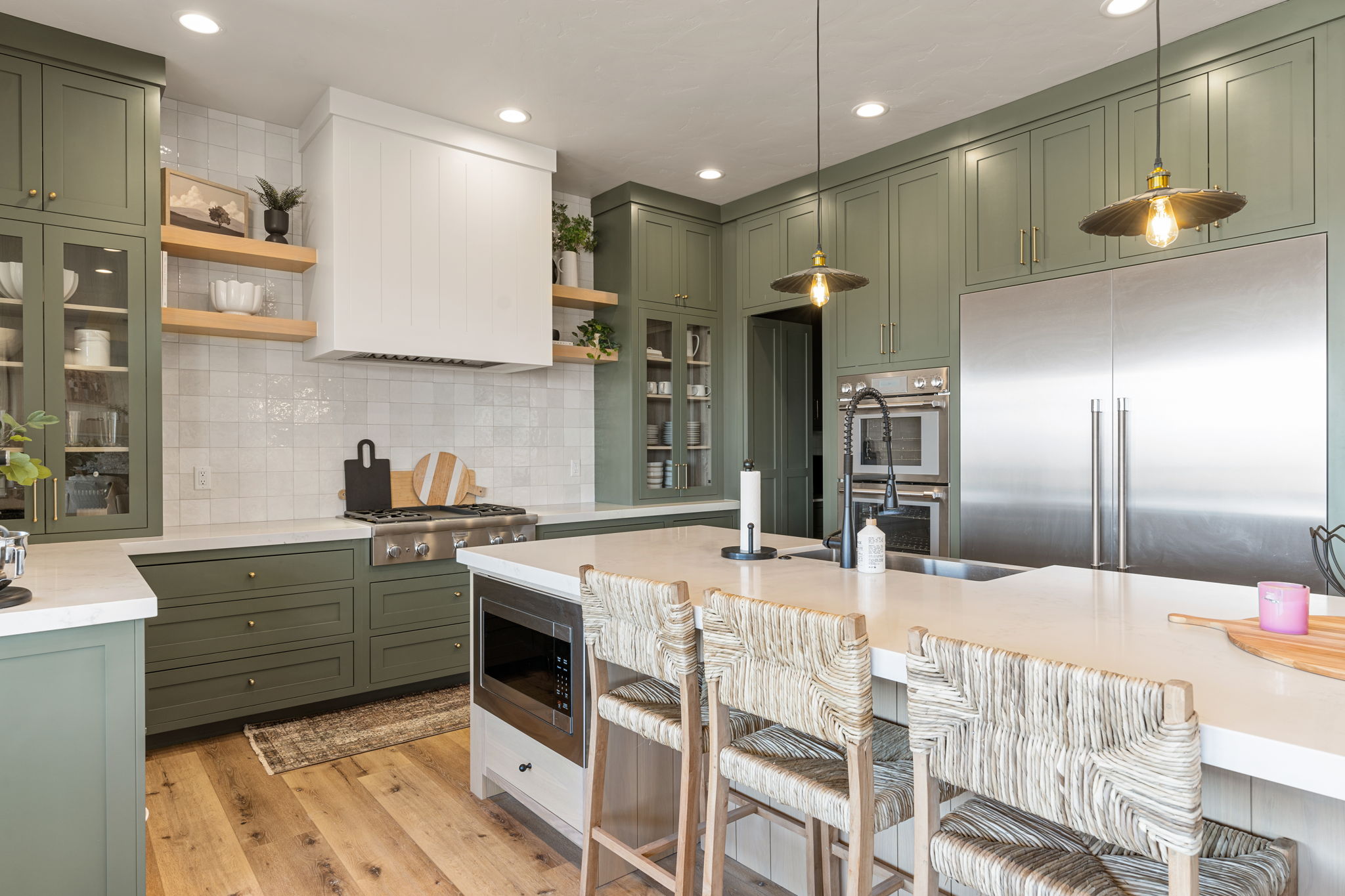 Kitchen featuring sage green cabinetry, stainless steel appliances, a large center island with integrated microwave, wood-finish flooring, and a white tile backsplash