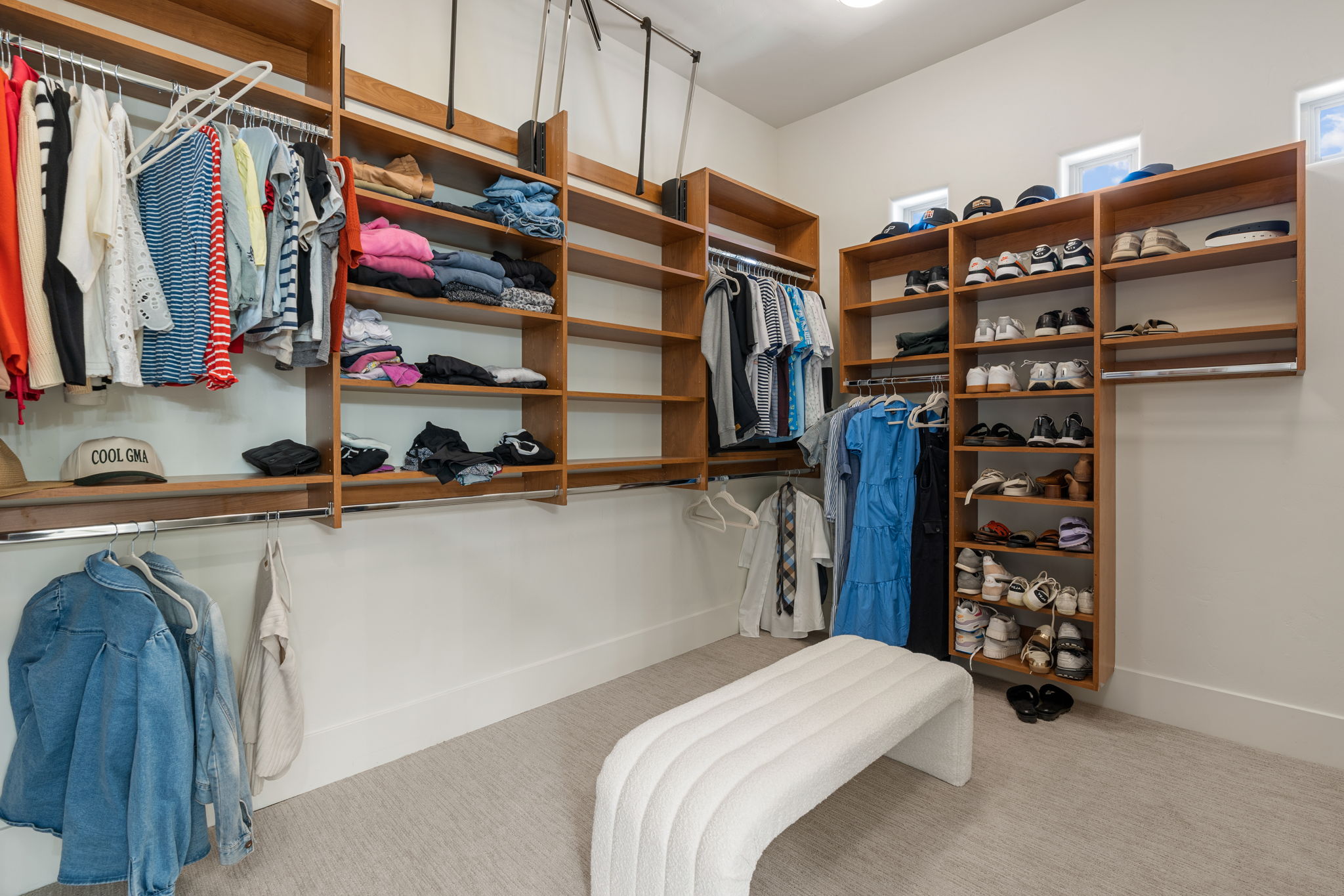 Spacious walk-in closet featuring extensive built-in wood shelving, multiple hanging rods, recessed ceiling lighting, and upper windows providing natural light