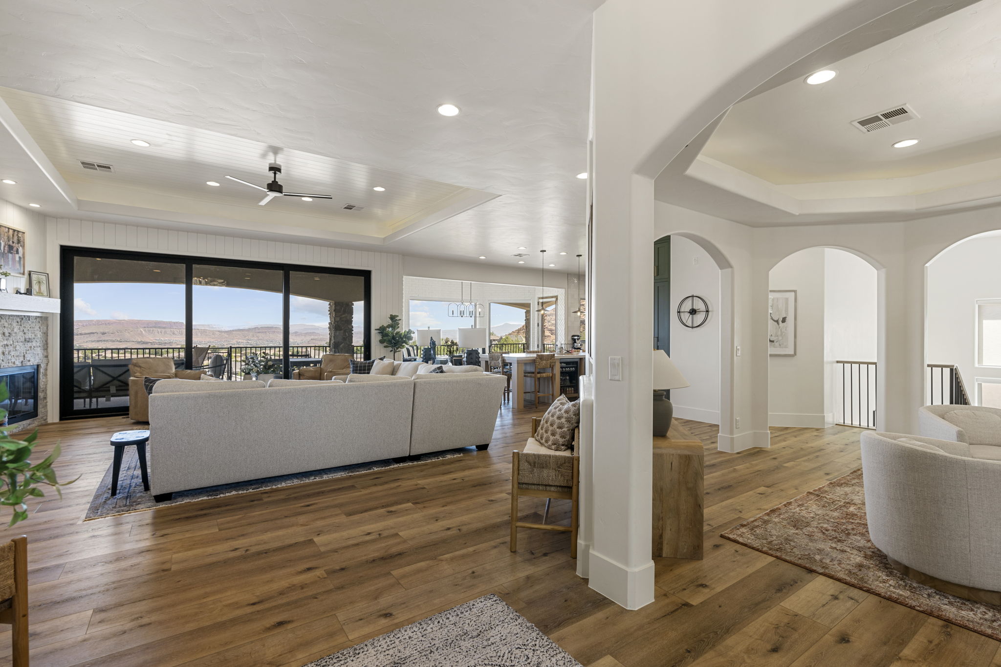 Spacious living area featuring wood-finish flooring, a stone-faced fireplace, and a tray ceiling with recessed lighting