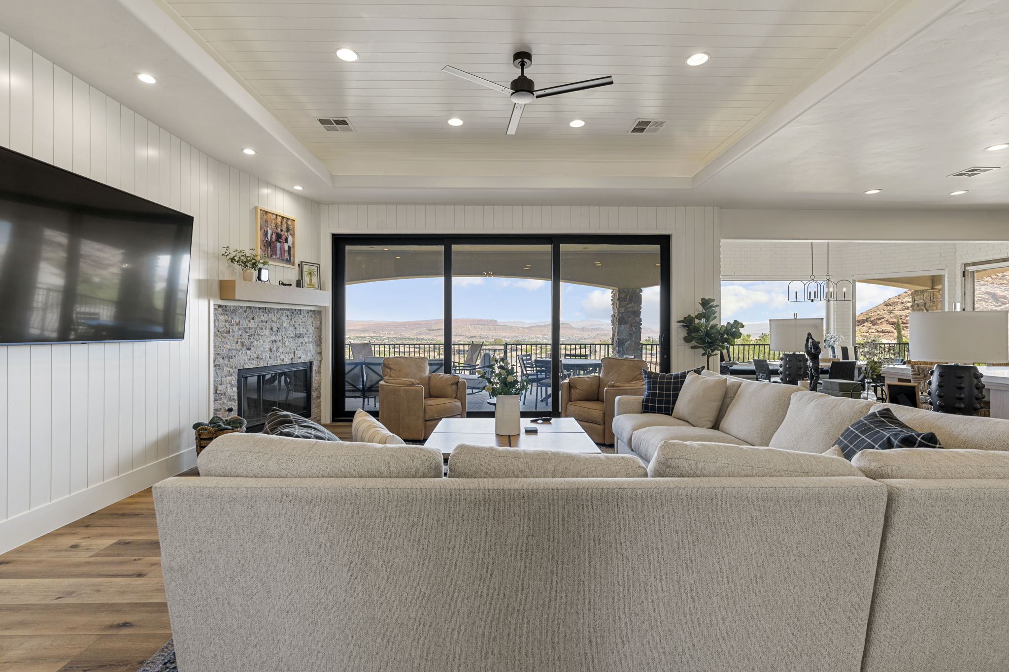Spacious living area featuring a wood-finish flooring, a contemporary fireplace with a stone surround and wood mantle, and white shiplap accent walls