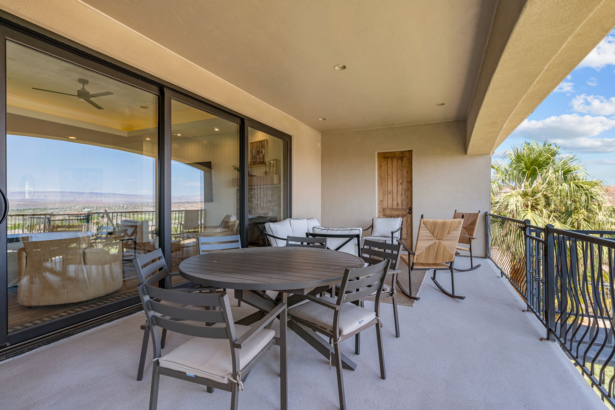 Expansive covered balcony featuring a textured concrete floor, black wrought iron railing, and a rustic wood door