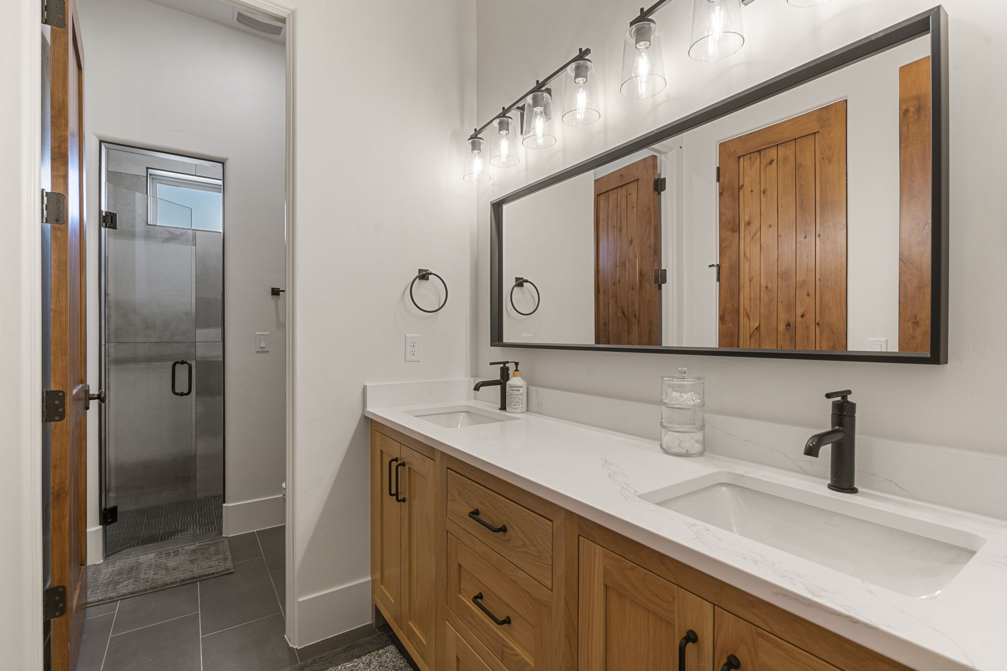 Dual vanity featuring wood-finish cabinetry, white countertops, and matte black fixtures