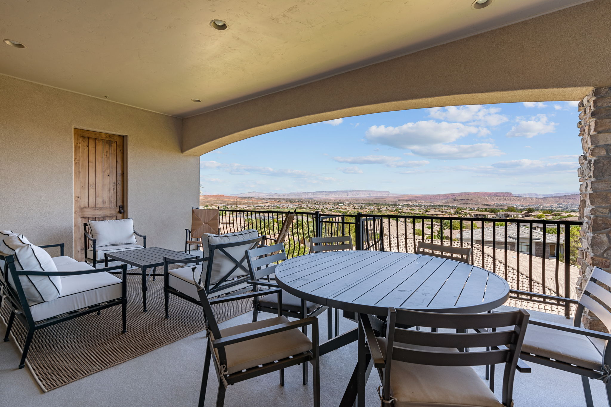 Covered patio featuring an arched entryway, stone veneer column, and wrought iron railing
