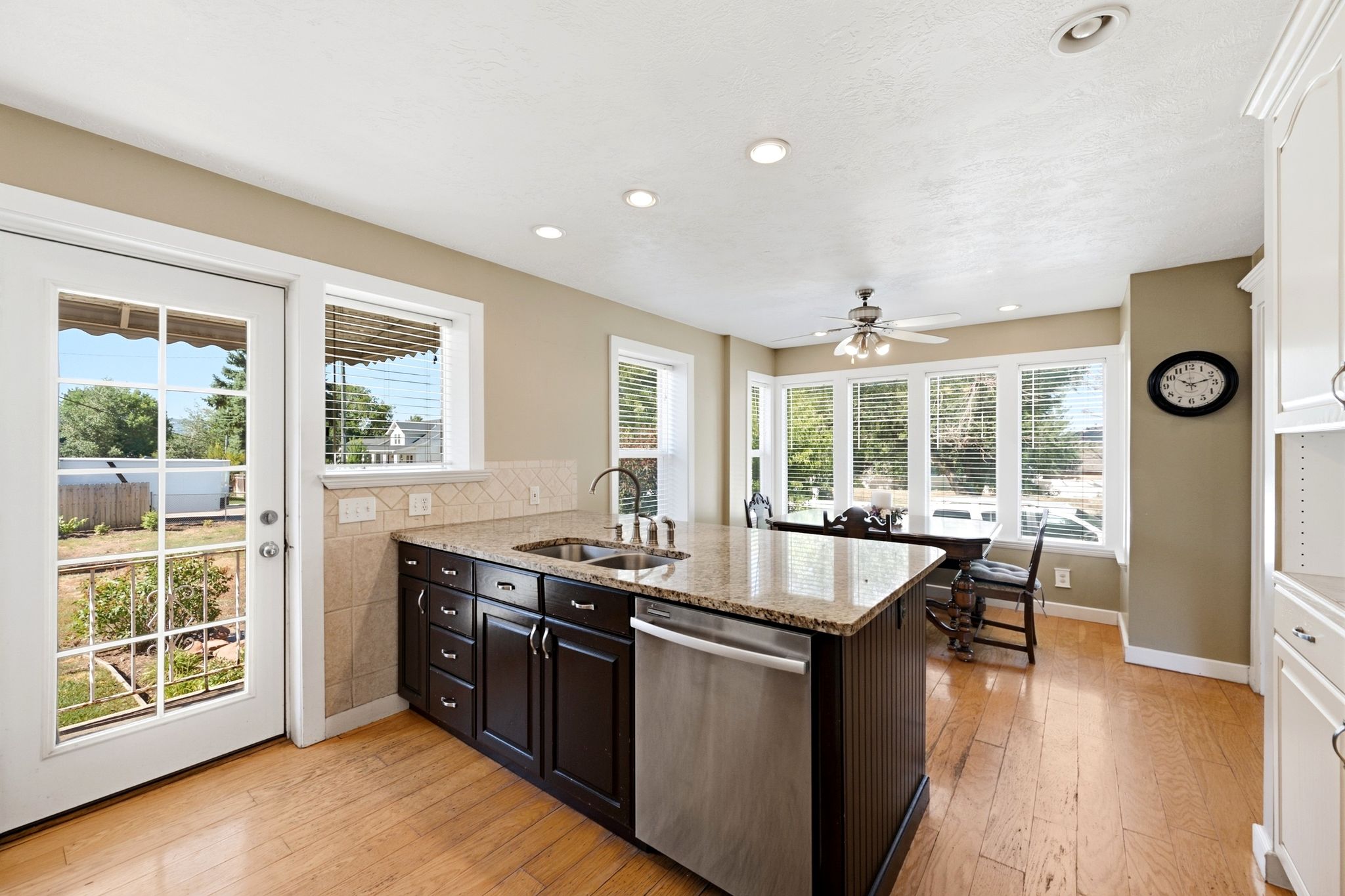 Kitchen featuring a center island with sink and stainless steel dishwasher, granite-finish countertops, tiled backsplash, and recessed lighting
