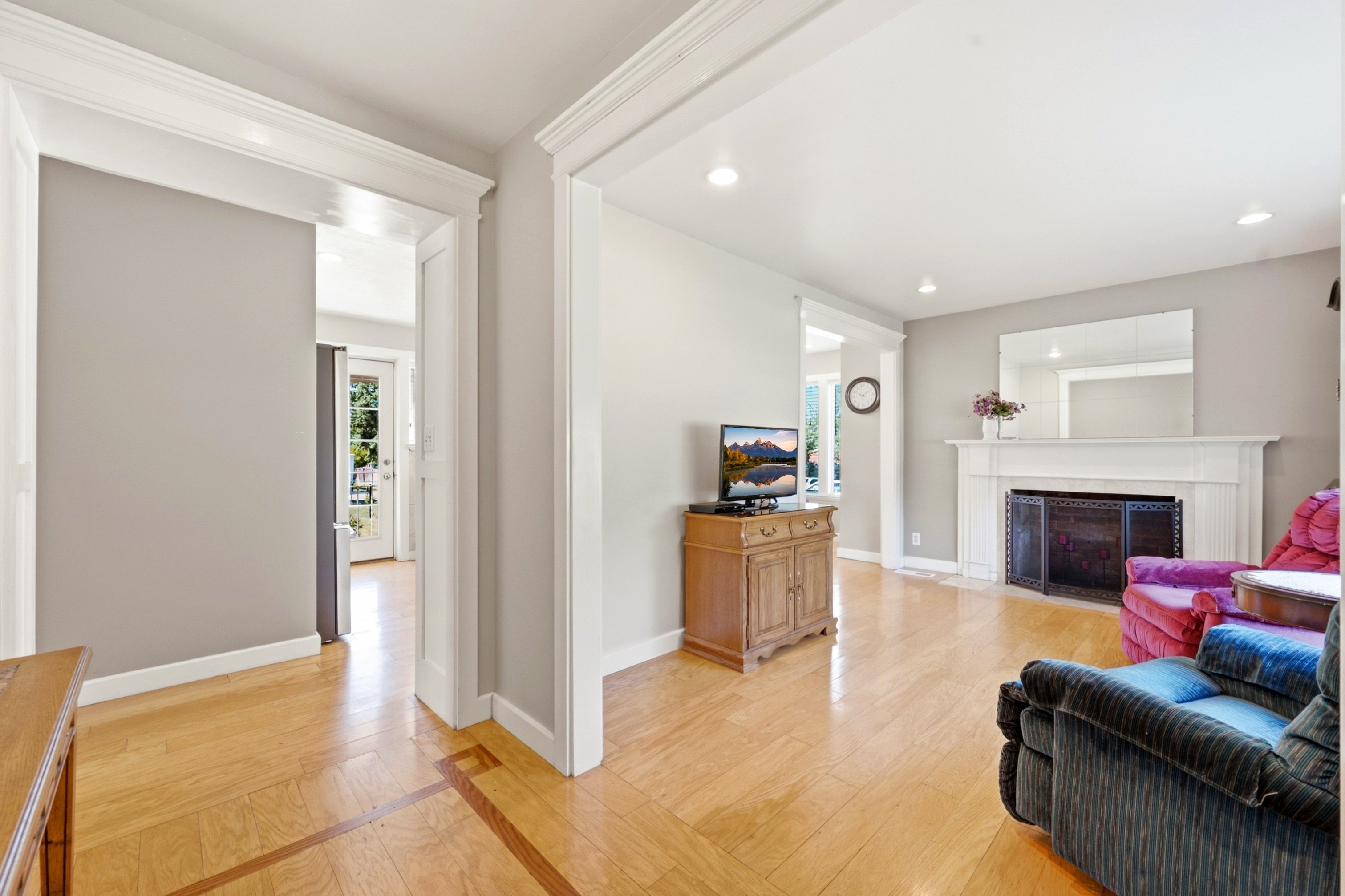 Spacious living area featuring light wood-finish flooring, recessed lighting, and a prominent fireplace with a white mantel and dark metal screen