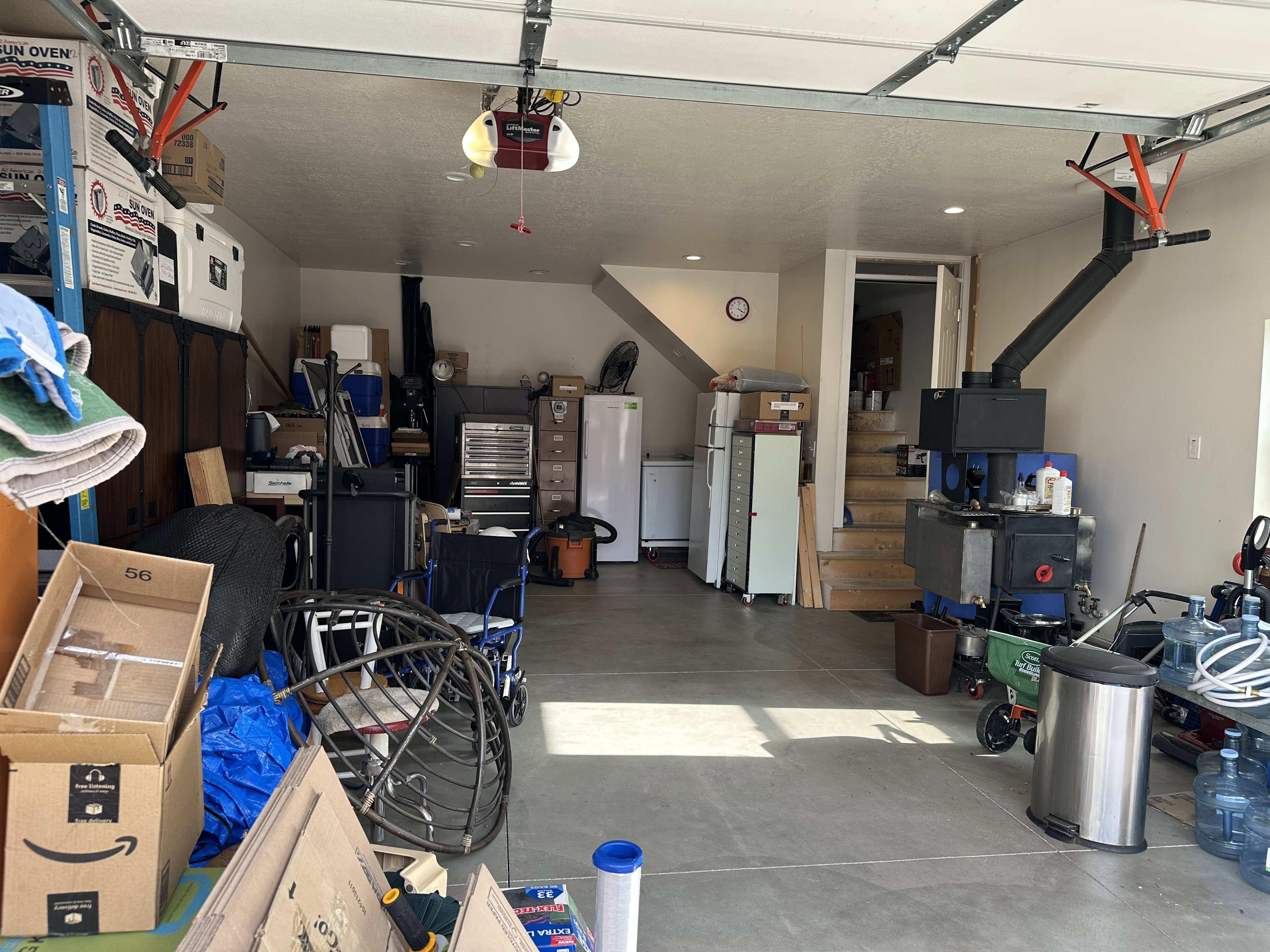 Attached garage with a concrete floor, overhead garage door system, recessed lighting, wood-burning stove, and loft staircase access