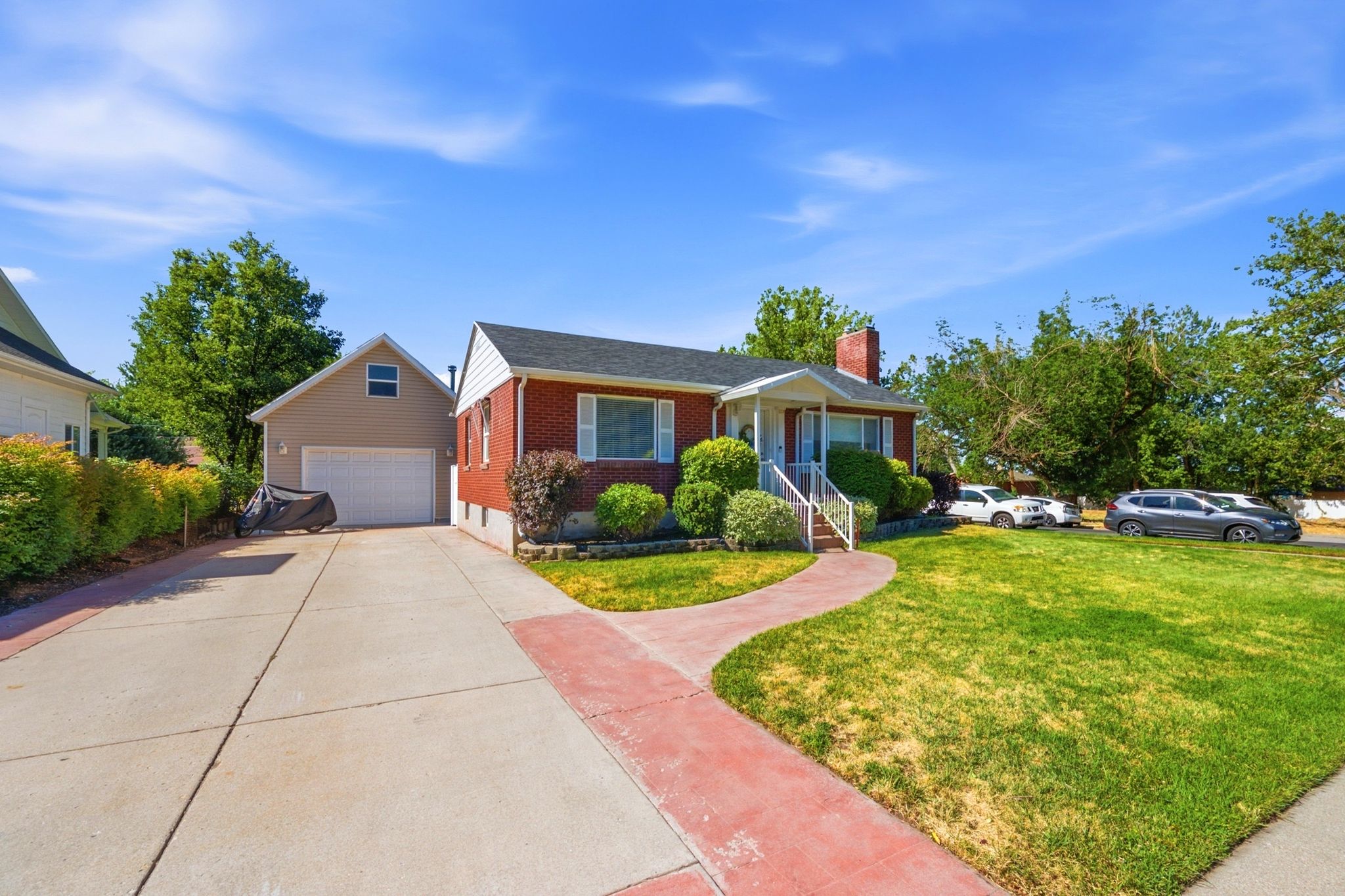 Brick residence featuring a covered front porch, red-toned walkway, and established landscaping