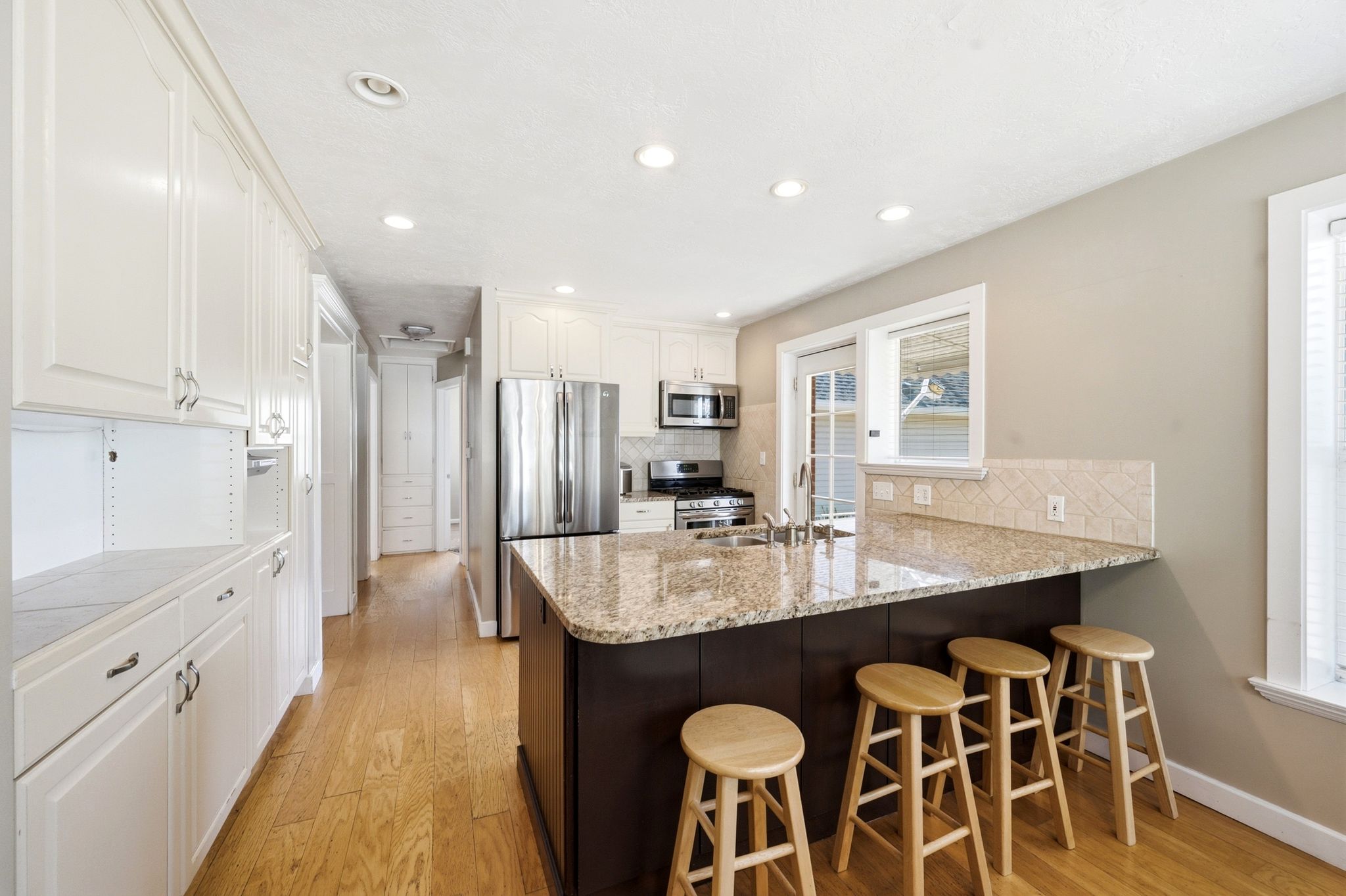 Modern kitchen featuring wood-finish flooring, white cabinetry, stainless steel appliances, and a central island with a granite countertop and integrated sink