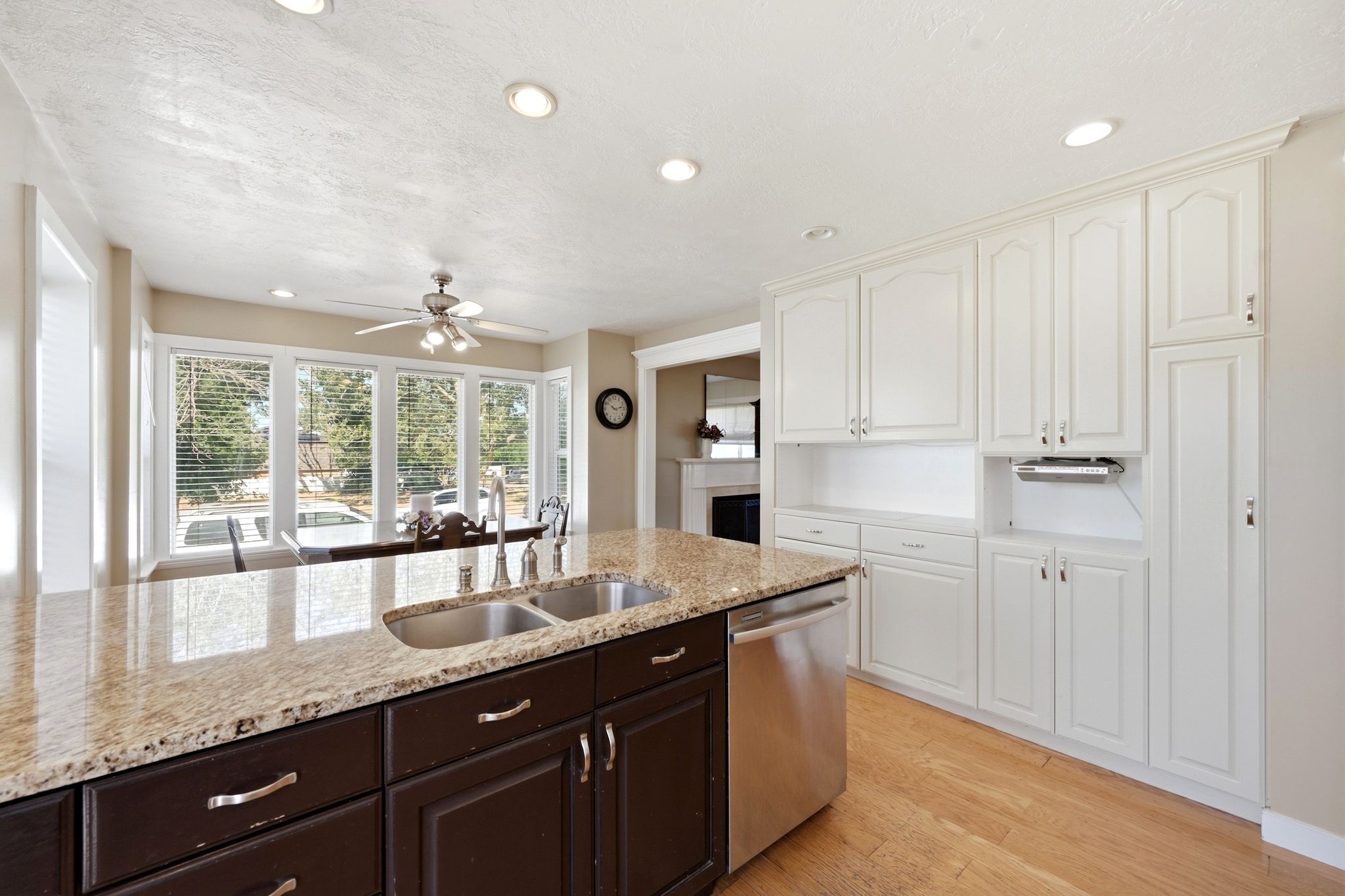 Kitchen featuring a central island with dual sinks, granite countertops, wood-finish flooring, recessed lighting, and white cabinetry