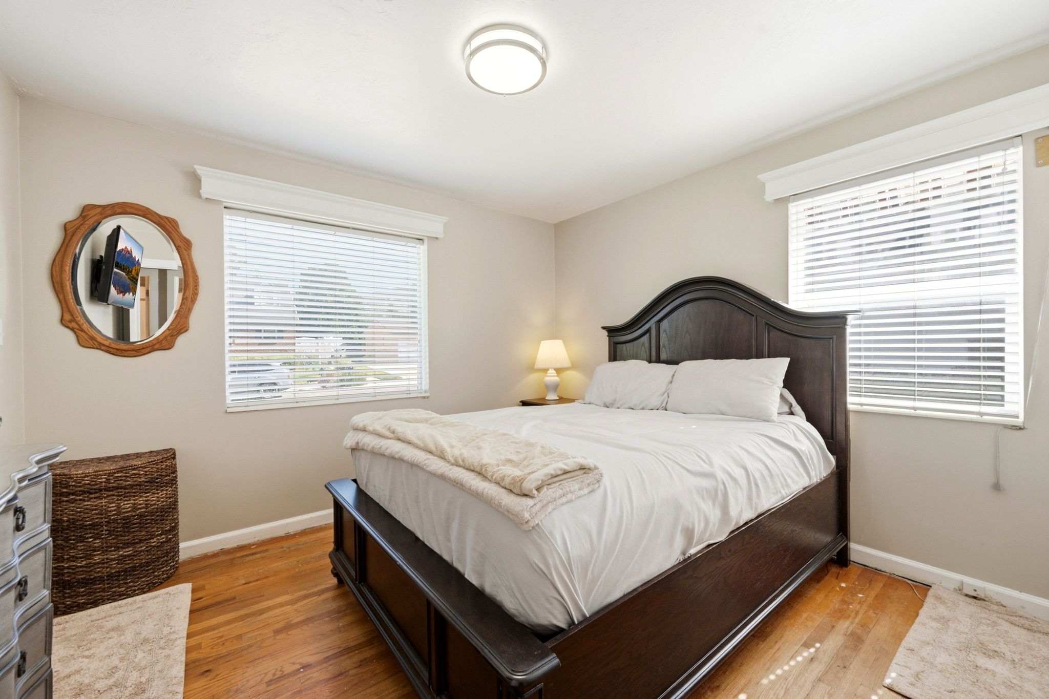 Bedroom featuring wood-finish flooring, two windows with blinds, a ceiling-mounted light fixture, and neutral wall tones