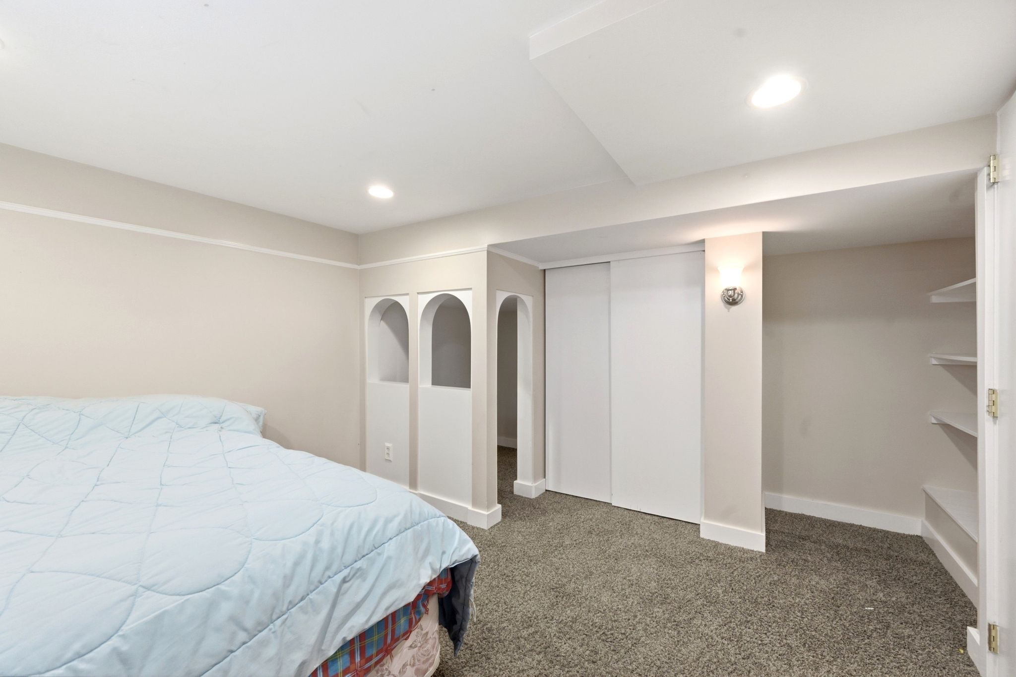 Recessed lighting illuminates a room featuring light-colored walls and carpeted flooring