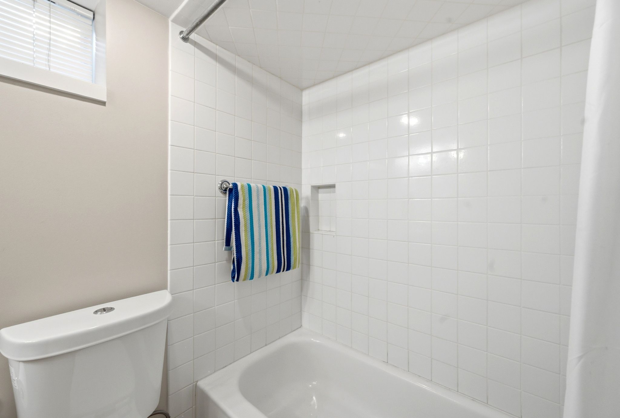 Bathroom featuring a white subway tile shower surround with an integrated niche, a white tub, and a white toilet