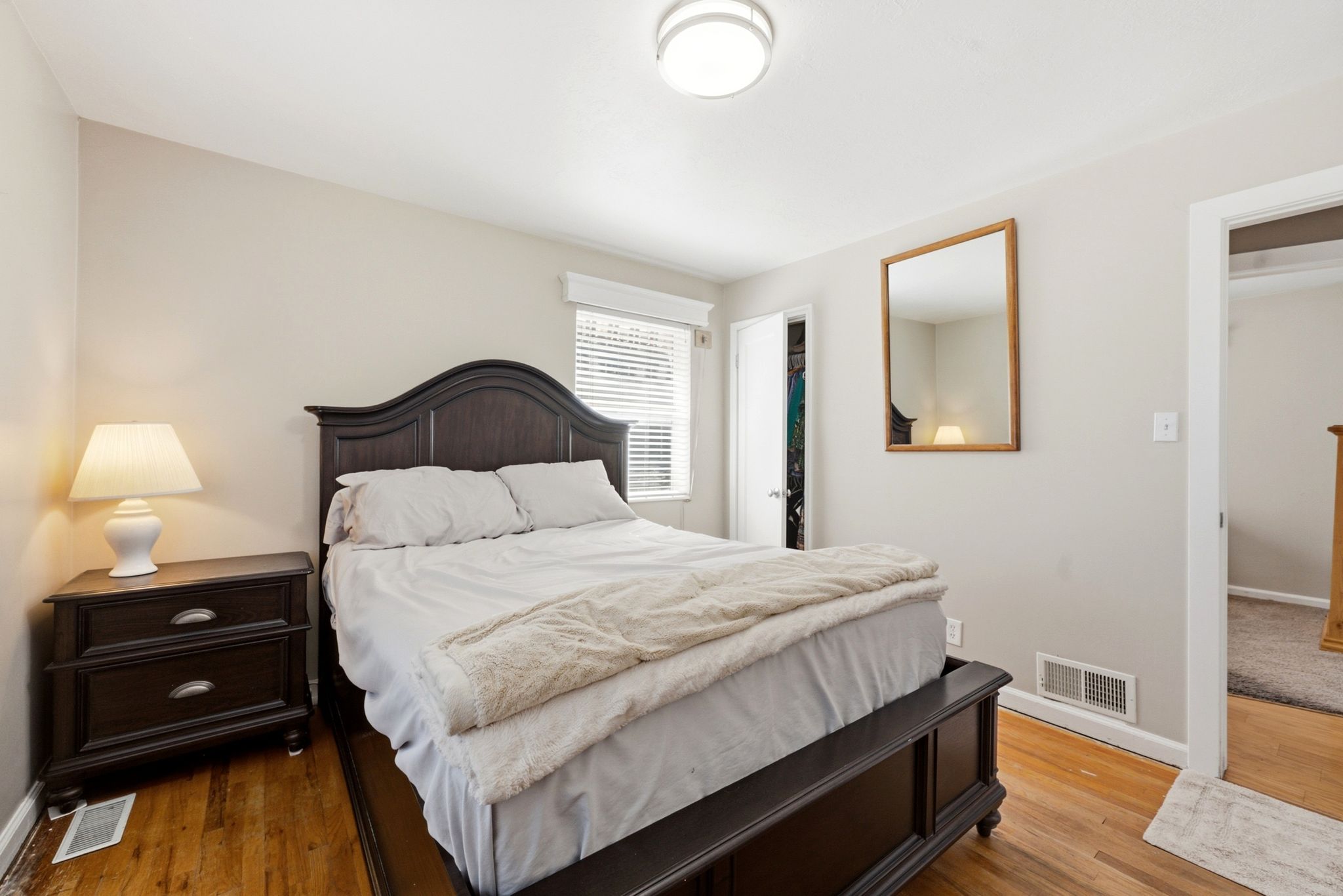 Bedroom featuring wood-finish flooring, light-toned walls, a ceiling-mounted light fixture, and a window with blinds