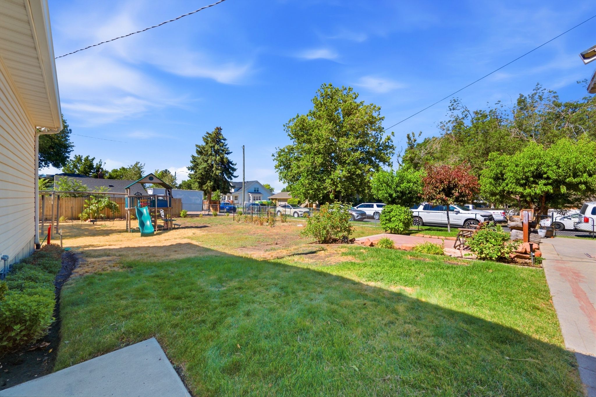 Expansive backyard featuring a combination of established lawn and landscaping, a concrete patio area, and a wood fence