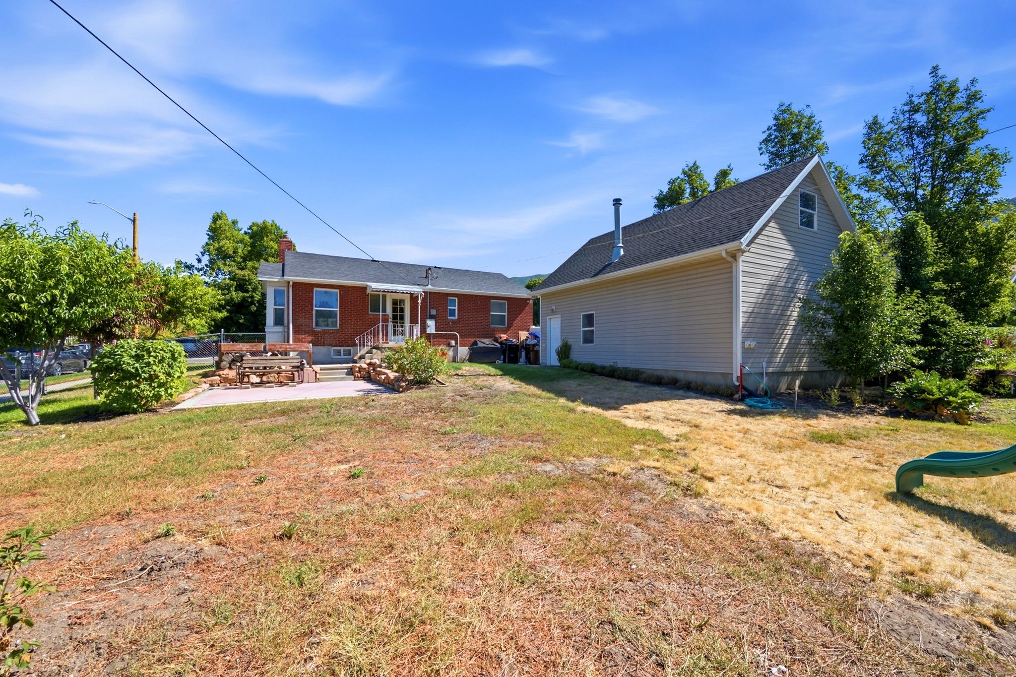 Expansive backyard featuring a brick exterior home with a patio, a separate detached structure with siding, and mature trees