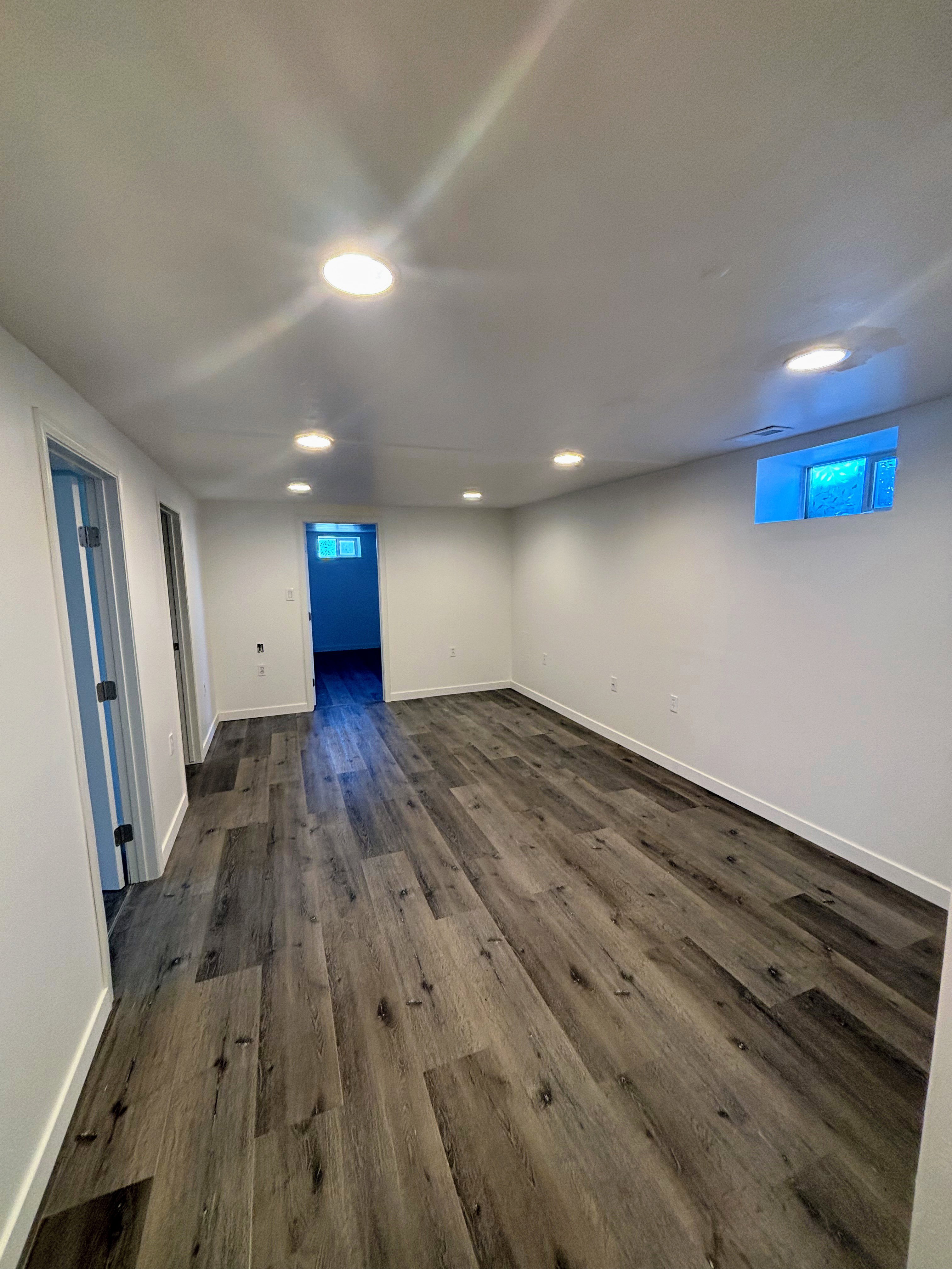 Spacious room featuring wood-finish flooring, white painted walls, recessed ceiling lighting, and a visible window