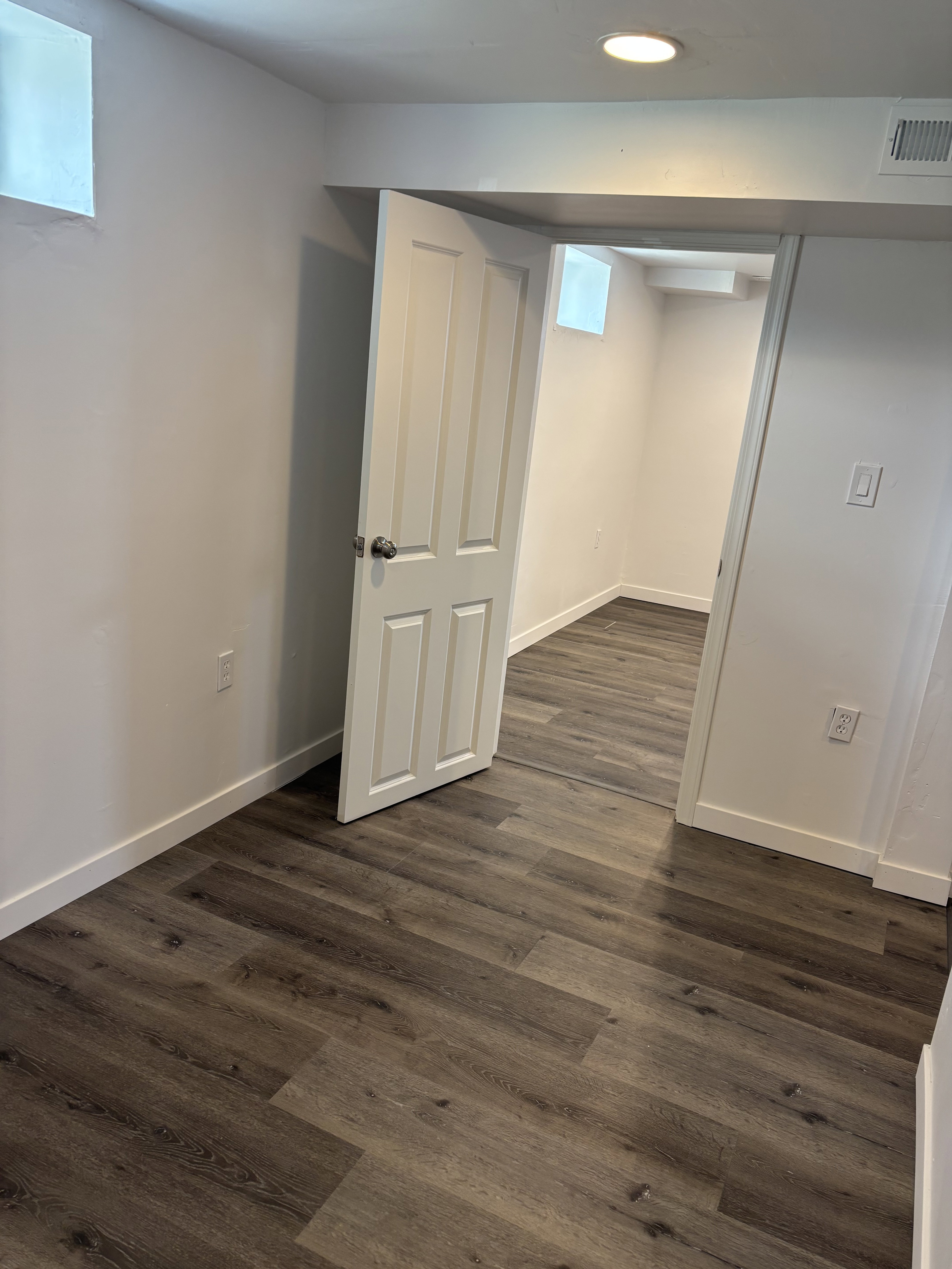 Interior room with wood-finish flooring, white painted walls, recessed lighting, and a white paneled door.