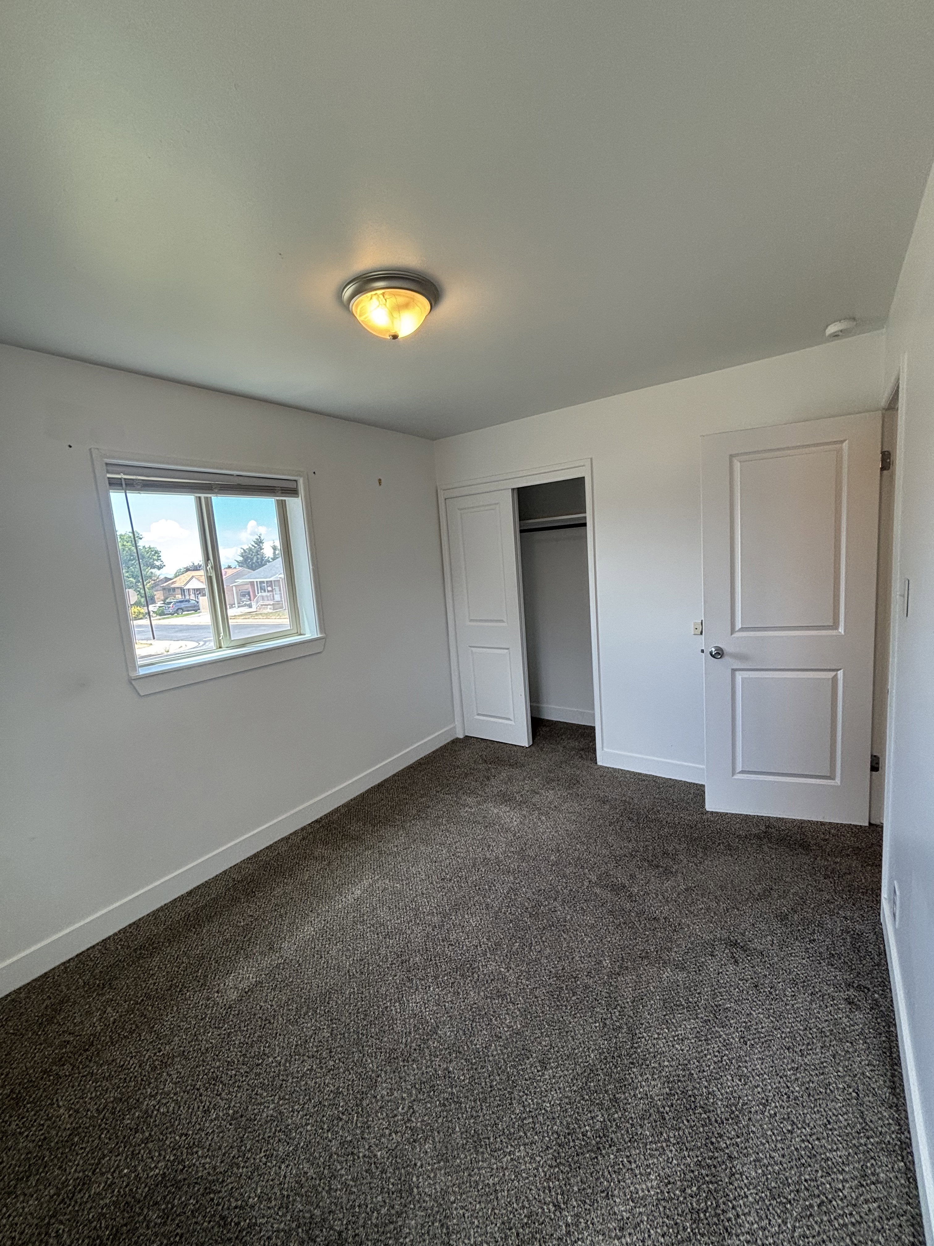Room featuring neutral wall paint, grey carpeting, a double-pane window, closet with sliding doors, and a flush-mount ceiling light fixture.