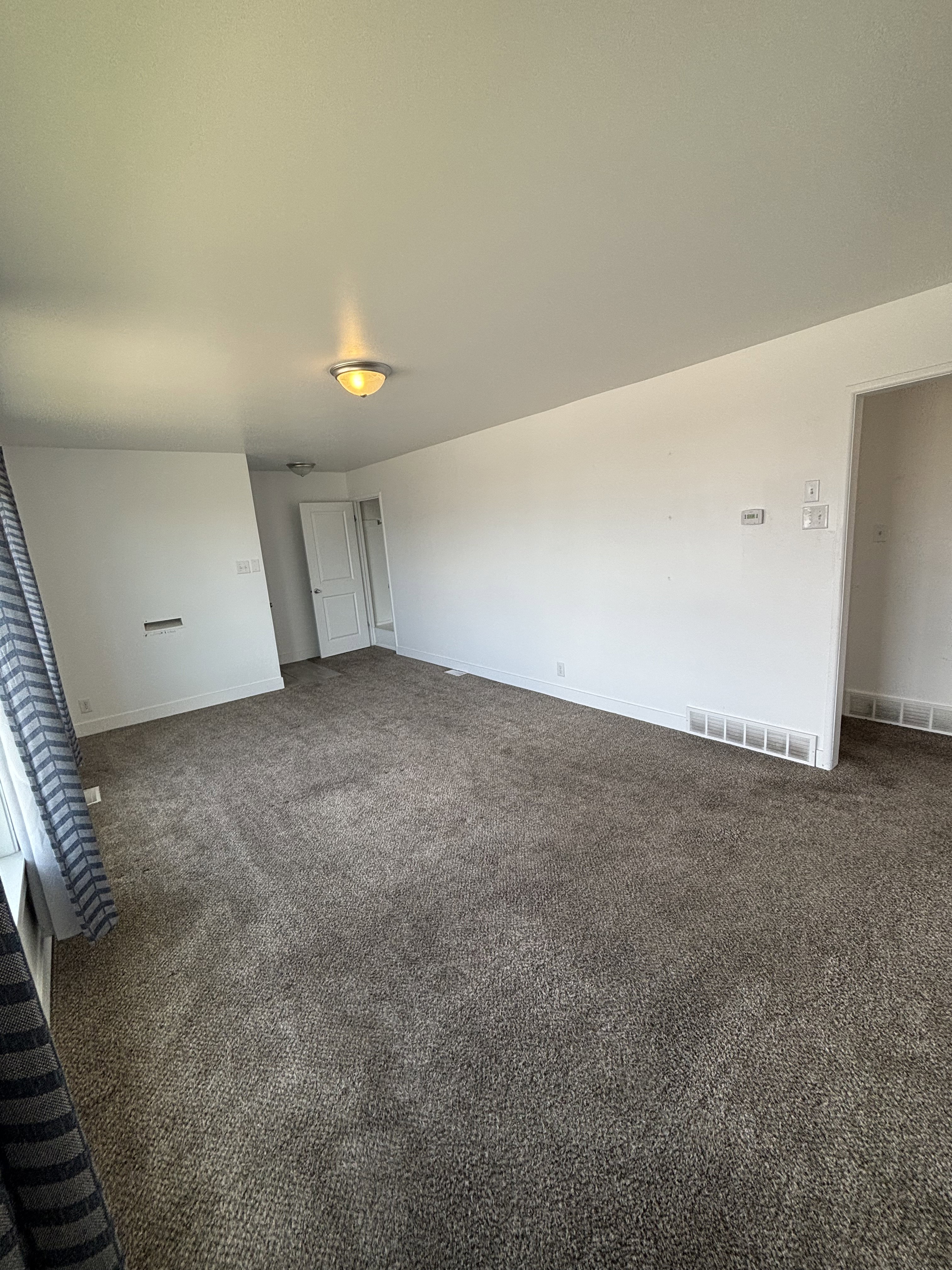 Spacious room featuring plush carpet flooring, white baseboards, and a semi-flush mount ceiling light fixture.