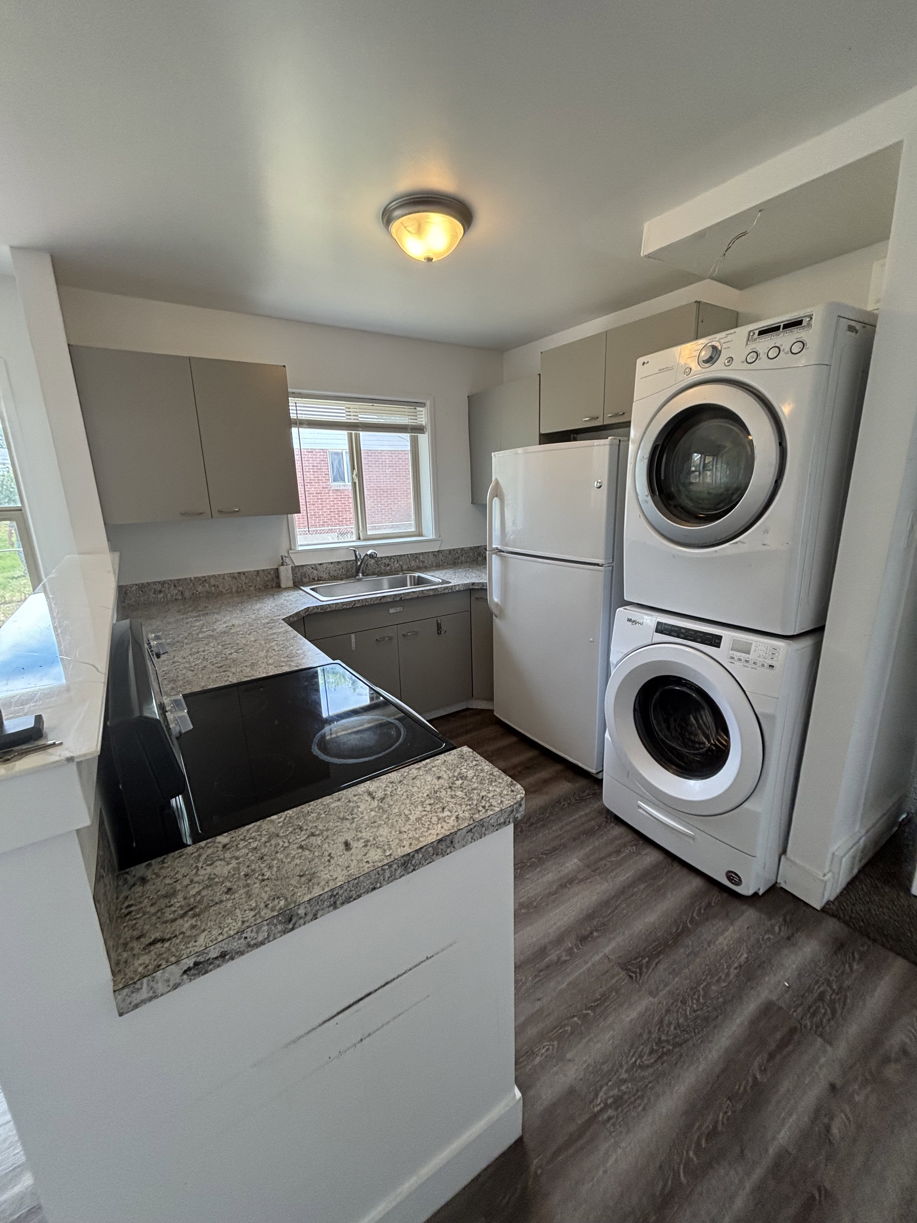 Compact kitchen featuring wood-finish flooring, light grey cabinetry, and a granite-pattern countertop.