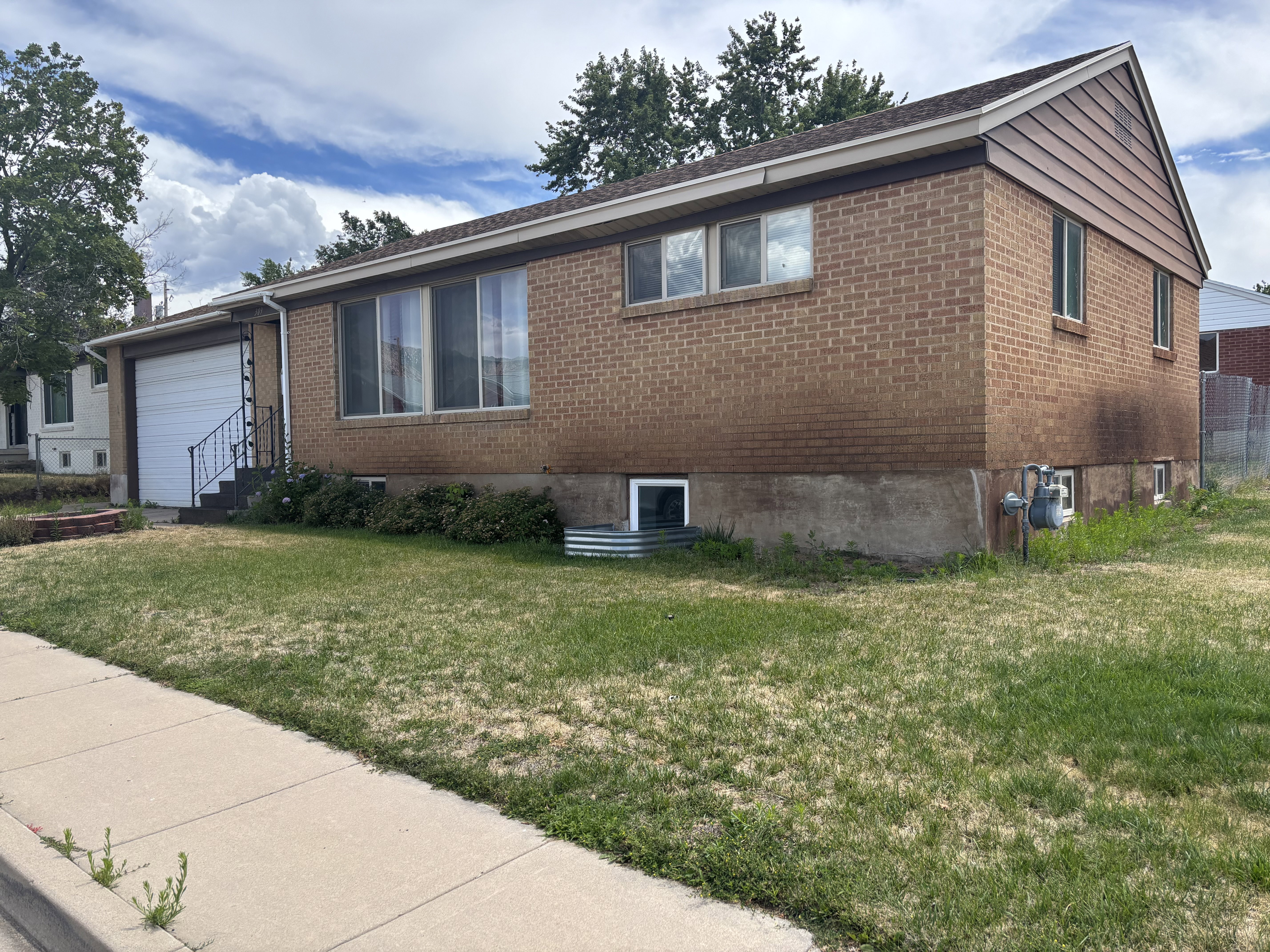 Brick exterior featuring a white garage door, concrete sidewalk, and established shrubbery/