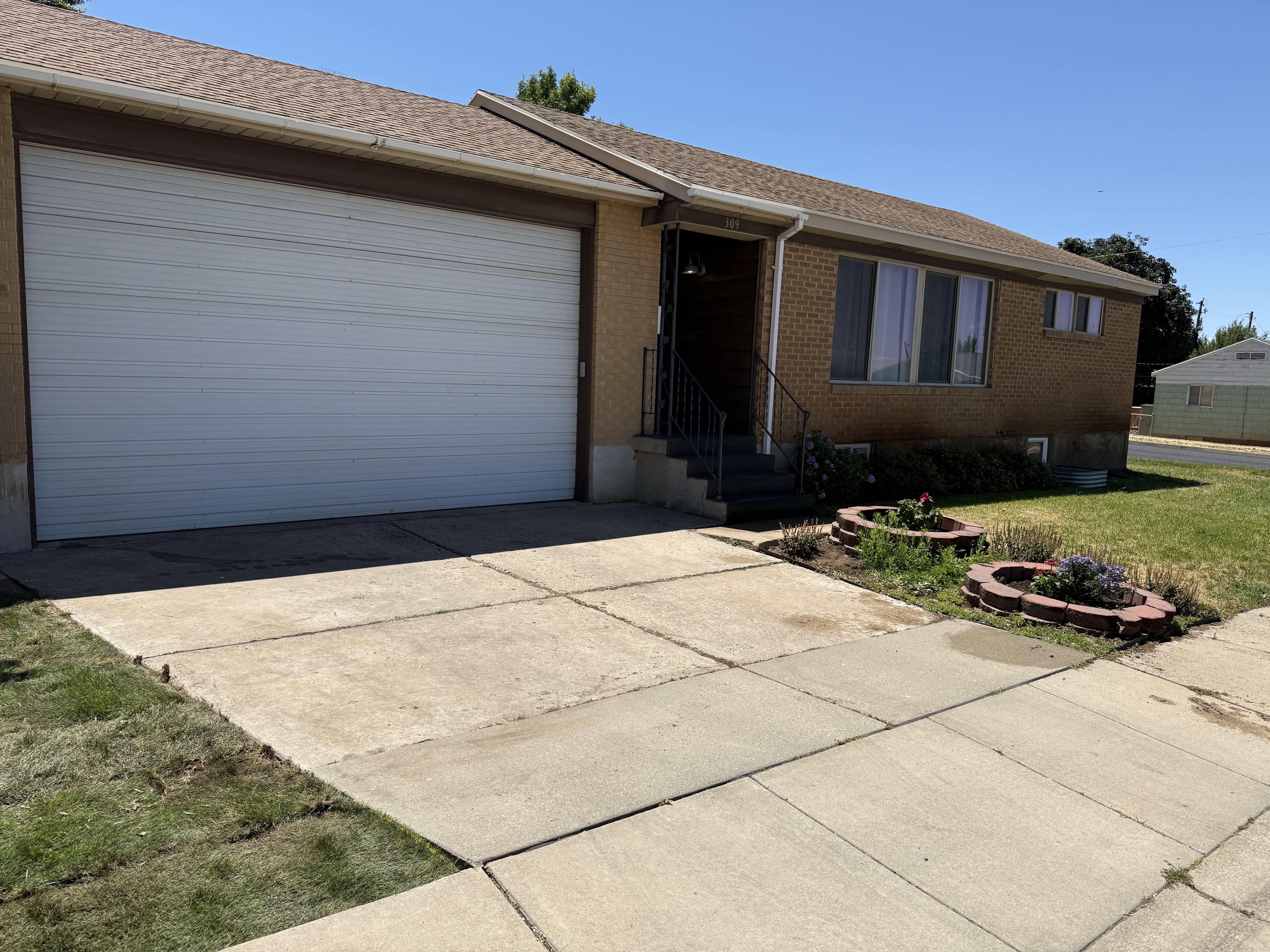 Brick facade residence featuring an attached garage with a white panel door, concrete driveway, and front entry with dark railings.