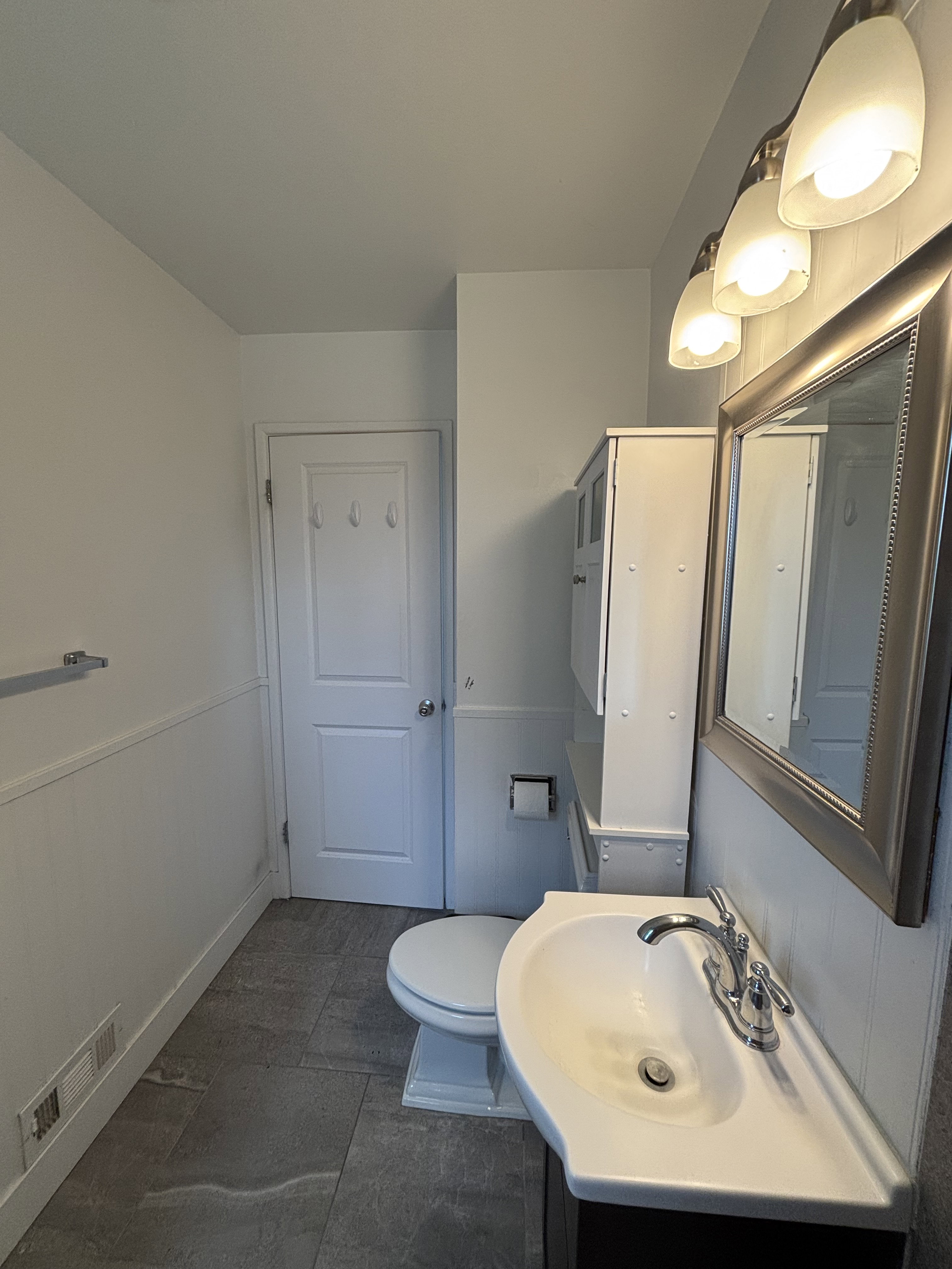 Bathroom featuring a pedestal sink with chrome faucet, a wall-mounted mirror, and a three-light vanity fixture.