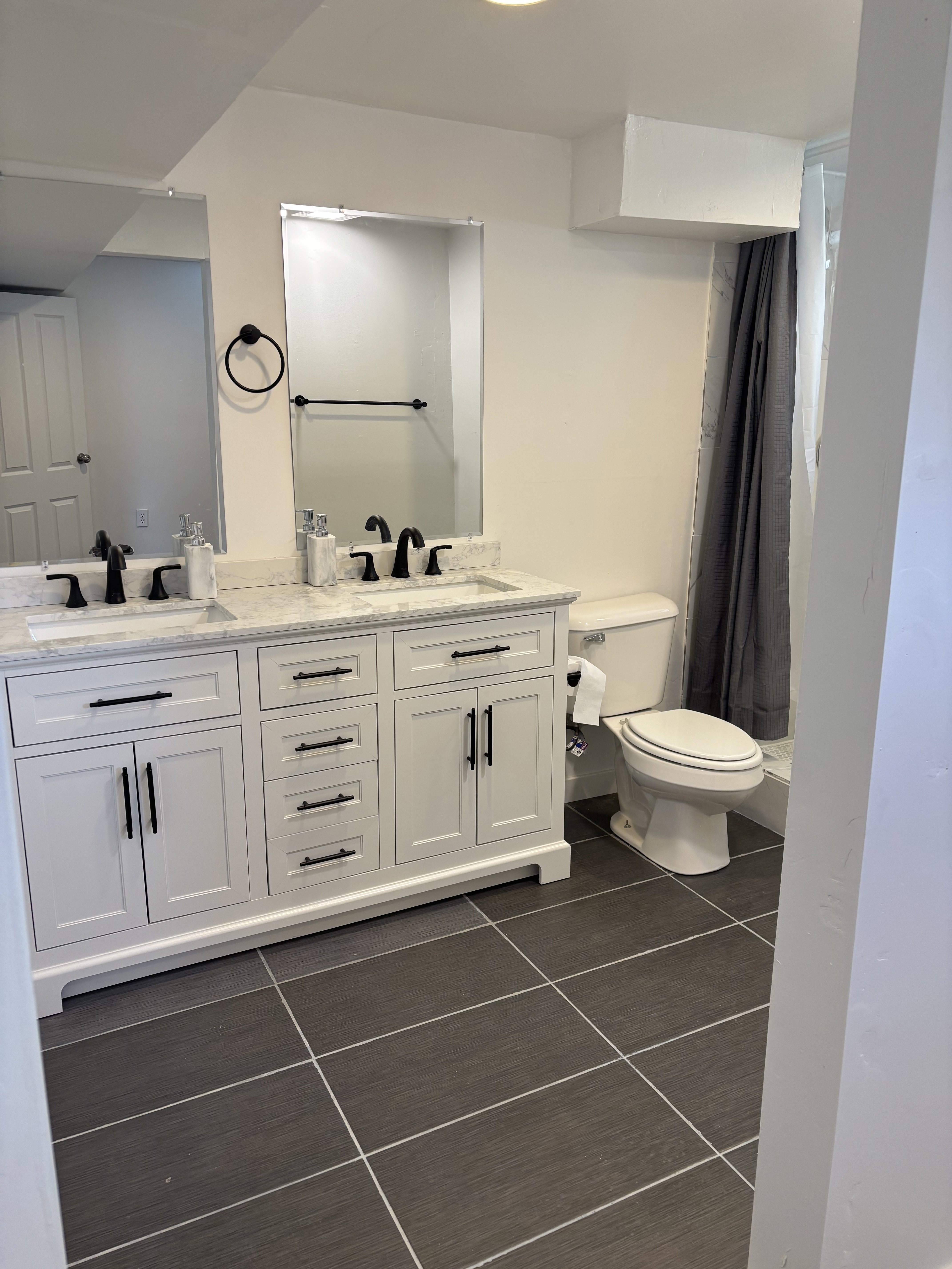 Bathroom featuring a double vanity with white cabinetry, light-toned countertops, and matte black fixtures.