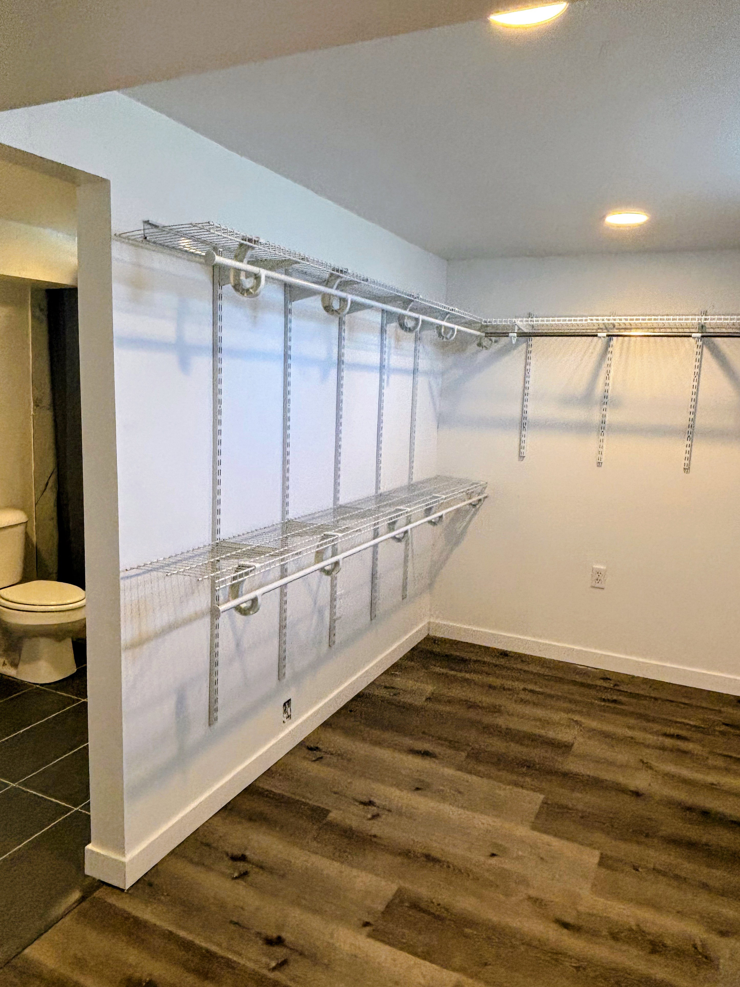 Walk-in closet with adjustable wire shelving, recessed lighting, and wood-finish flooring.